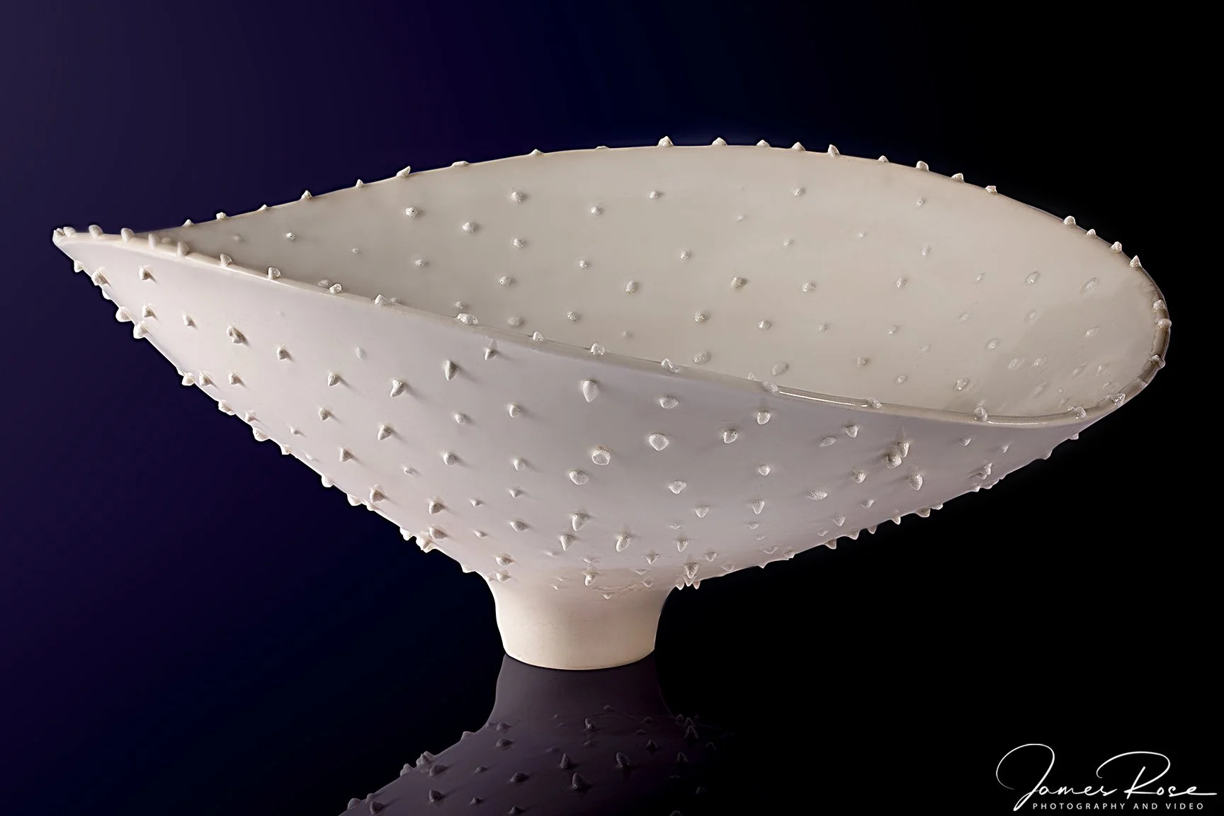 White ceramic bowl with small raised bumps, placed on a reflective black surface, against a dark background.