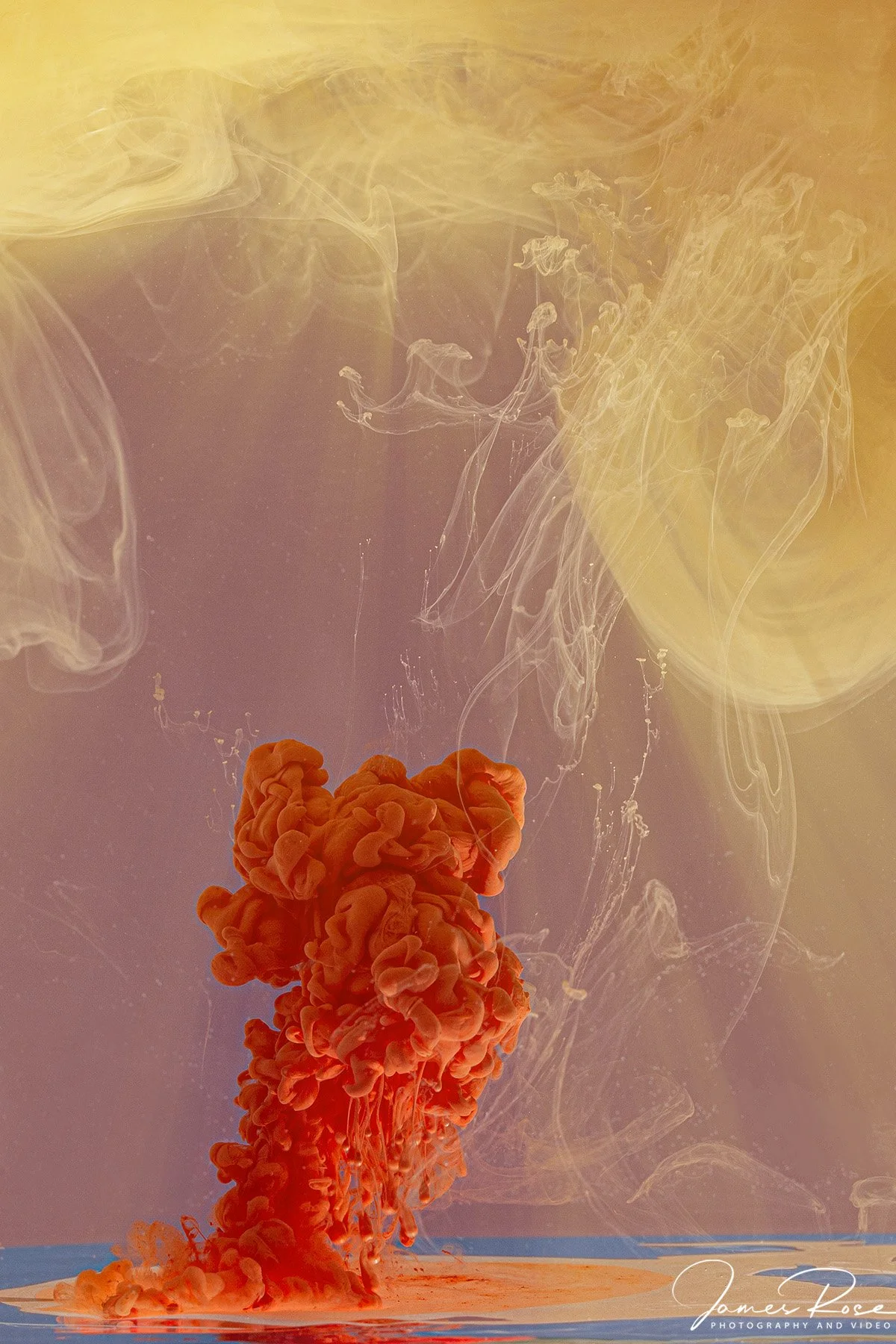 Colorful ink cloud dispersing in water with yellow and purple hues.