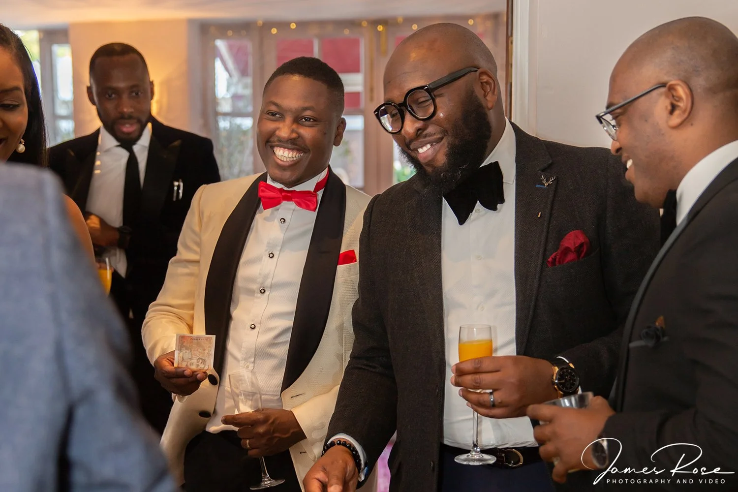 Group of well-dressed men and women socializing at a formal event, smiling and holding drinks, with a warmly lit background.