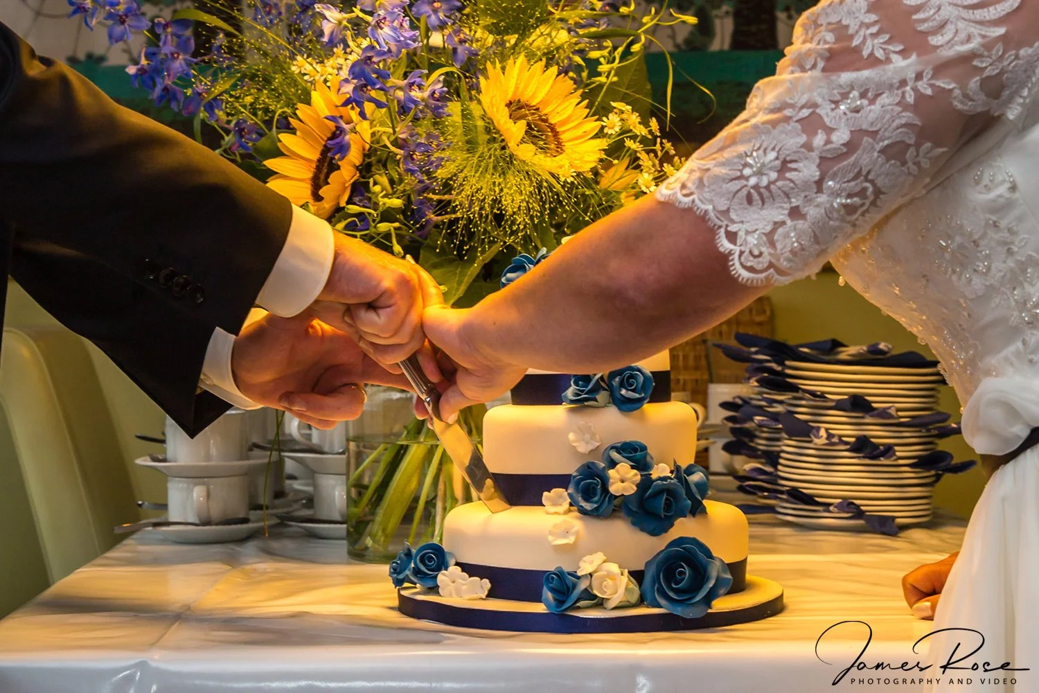 A bride and groom cutting a wedding cake together, with a bouquet of flowers in the background.
