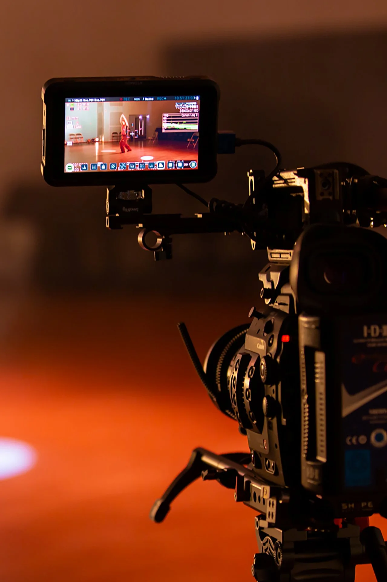 A professional video camera capturing a dancer performing on a stage, with the camera monitor showing the dancer's movements.