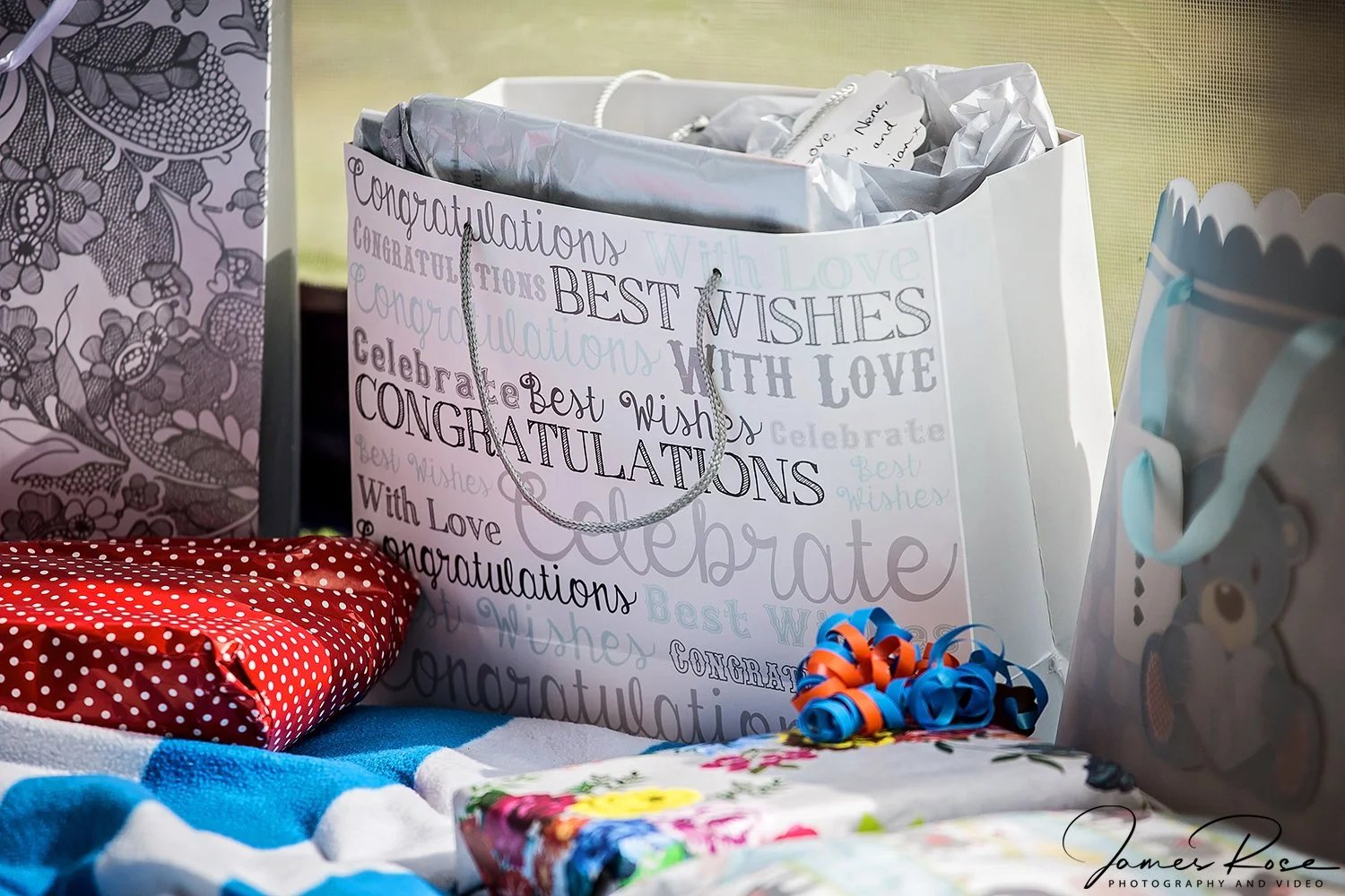 Gift bags with 'Congratulations' and 'Best Wishes' messages, wrapped presents, and decorative items on a table for a celebration.