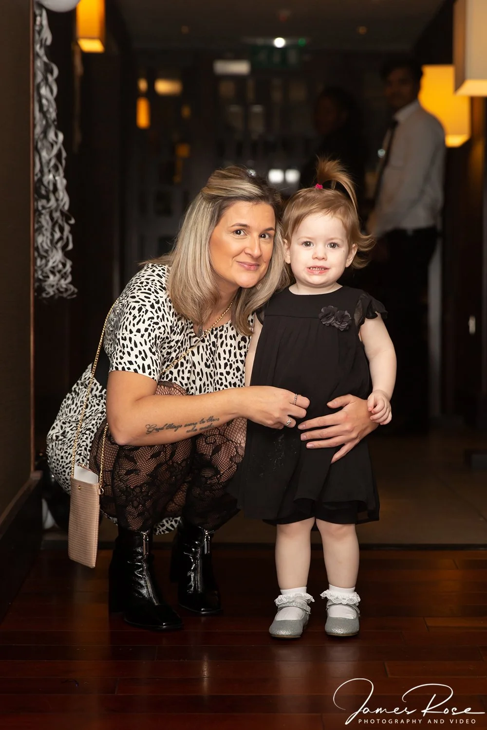 A woman with blonde hair and a young girl with light hair, dressed in black, posing together indoors at a social event.