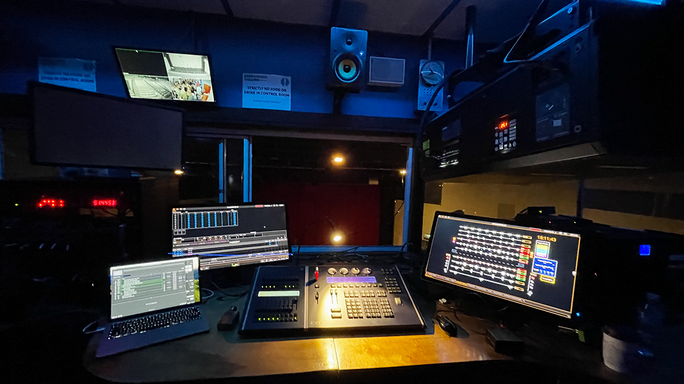 Lighting control room with multiple screens, audio equipment, and control panels in a dark environment.