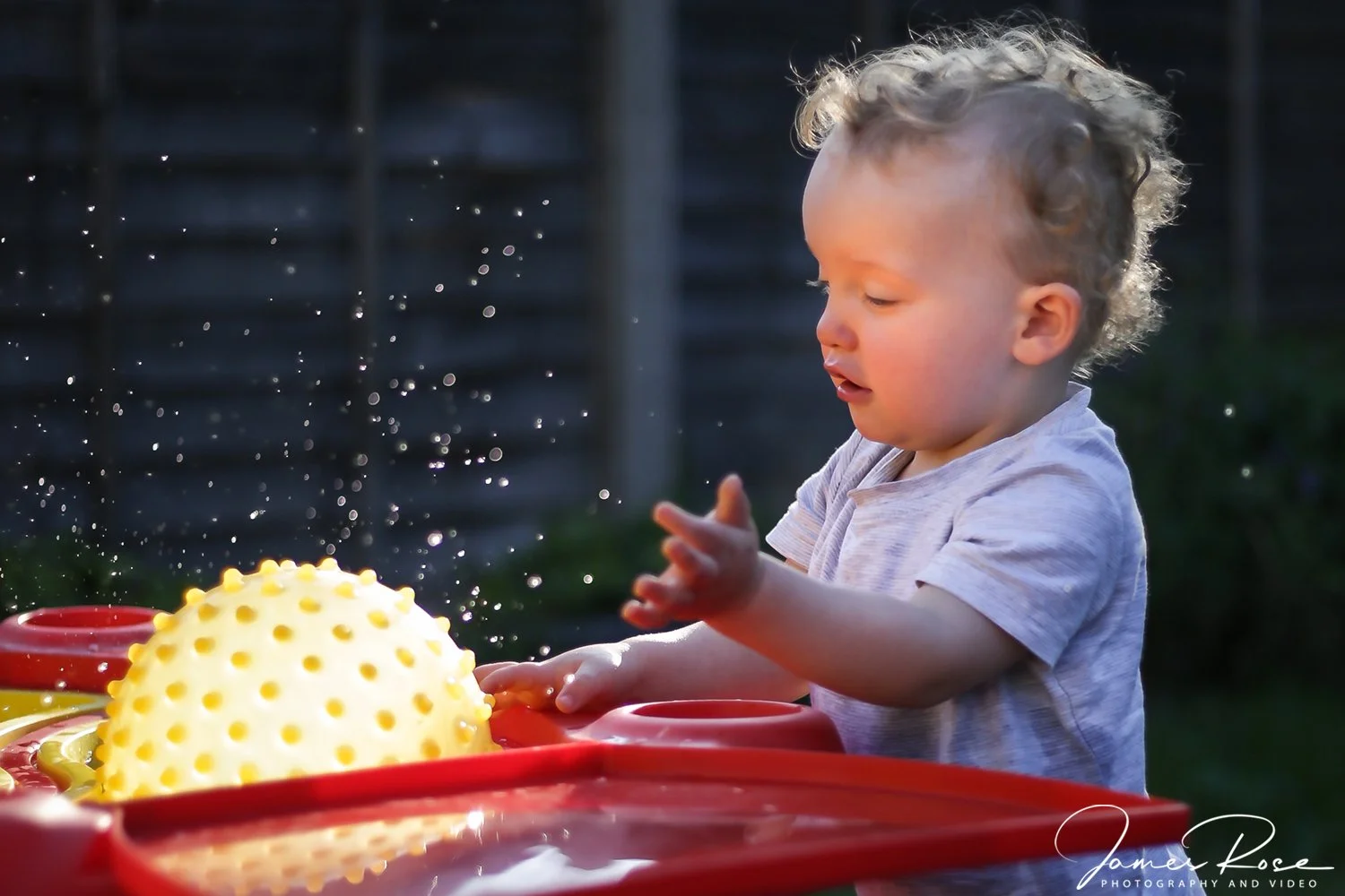 A young boy playing with a yellow textured ball outside on a sunny day.