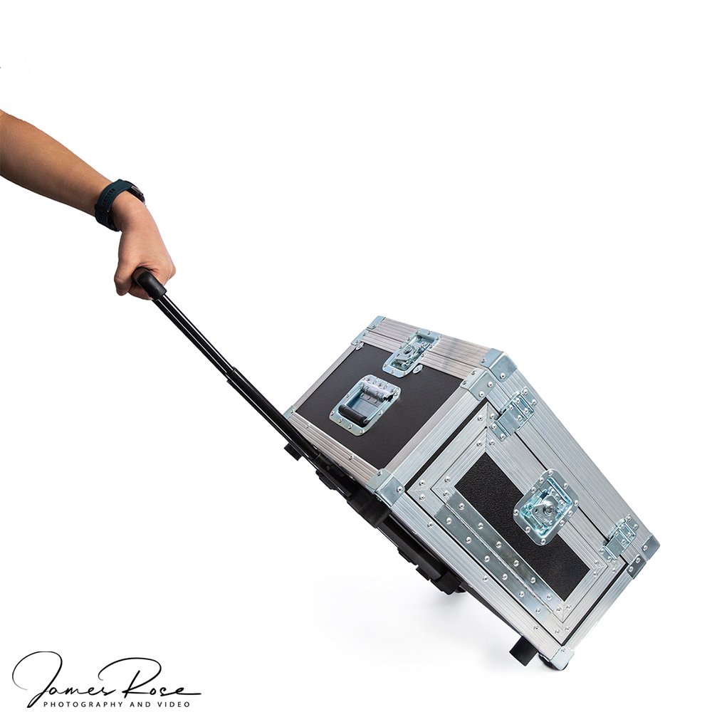 A person is pulling a silver and black portable equipment case on wheels with an extended handle
