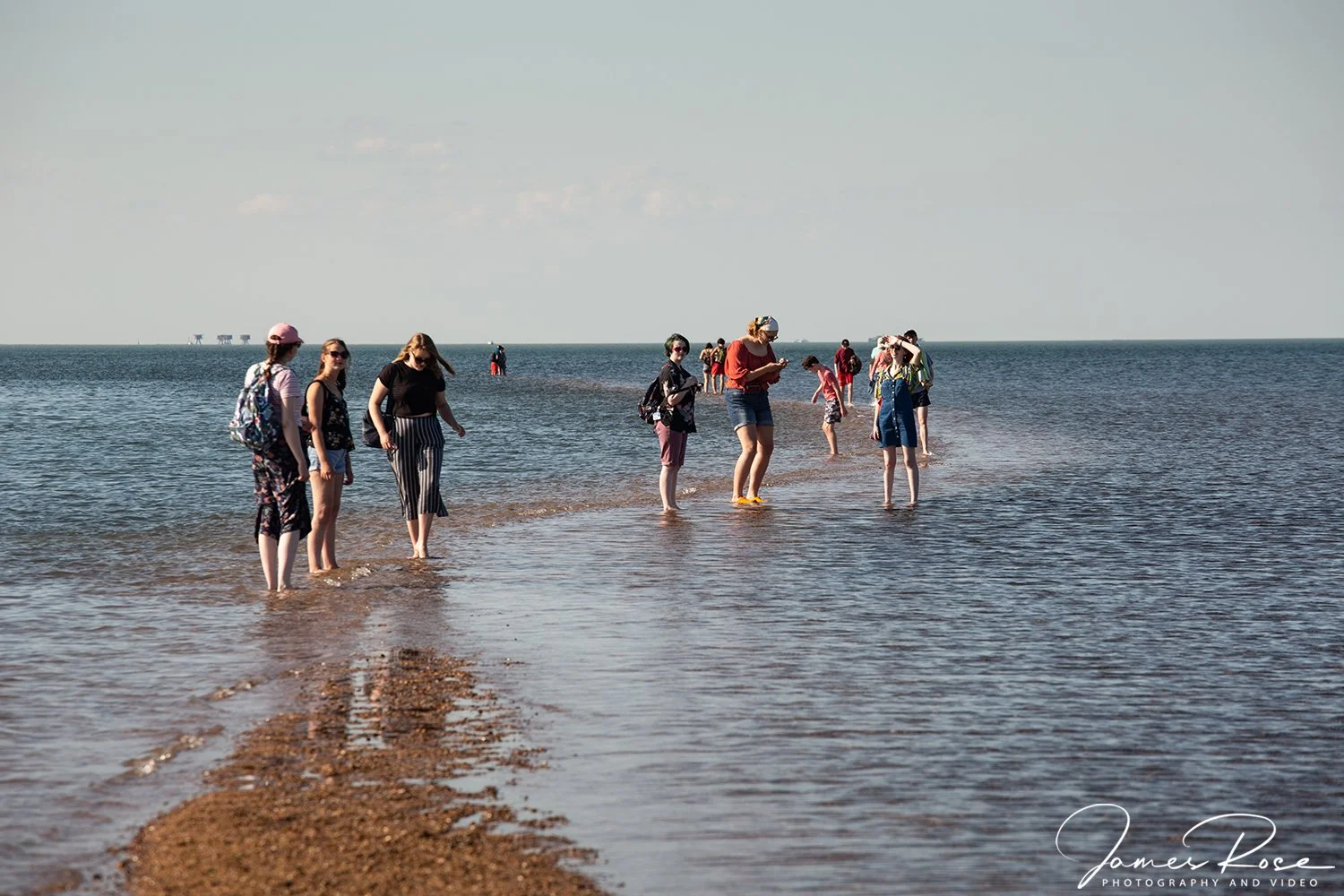 Group of people walking in shallow ocean water at the beach on a sunny day.