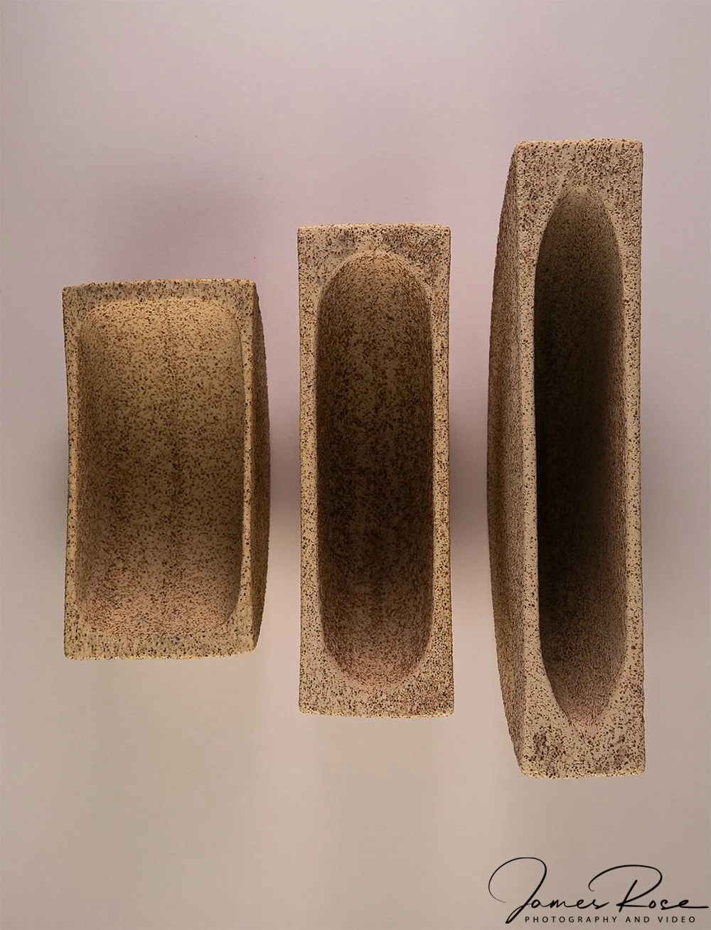 Three rectangular, sand-colored clay or concrete blocks with oval-shaped hollow centers, arranged in a row against a plain background.