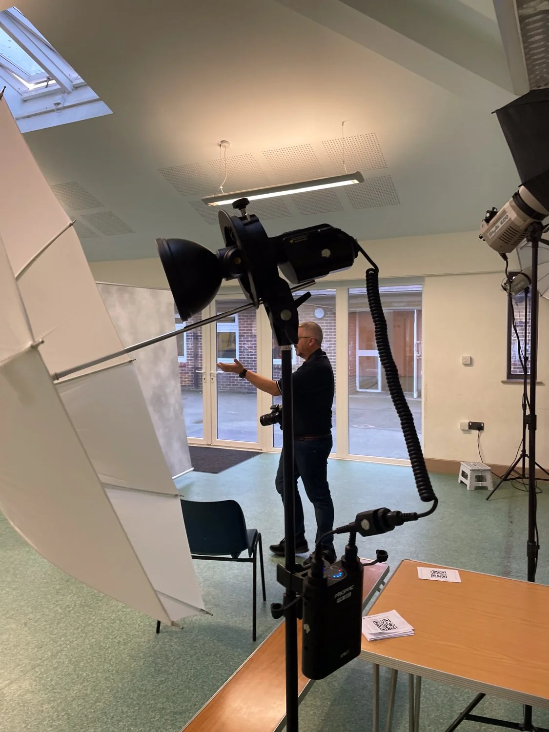 A man standing in a photography studio, gesturing with his hands, with professional lighting and backdrops around him.