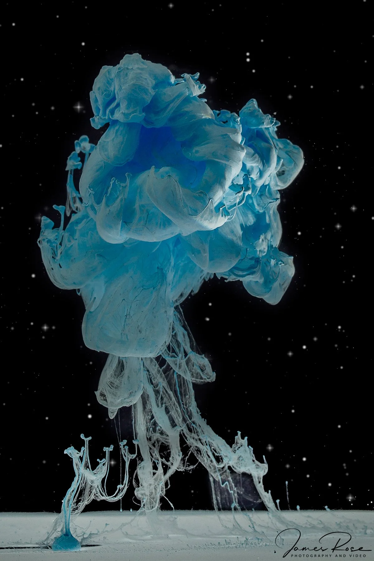 Blue and white ink in water forming abstract shapes against a black background with small white dots resembling stars.