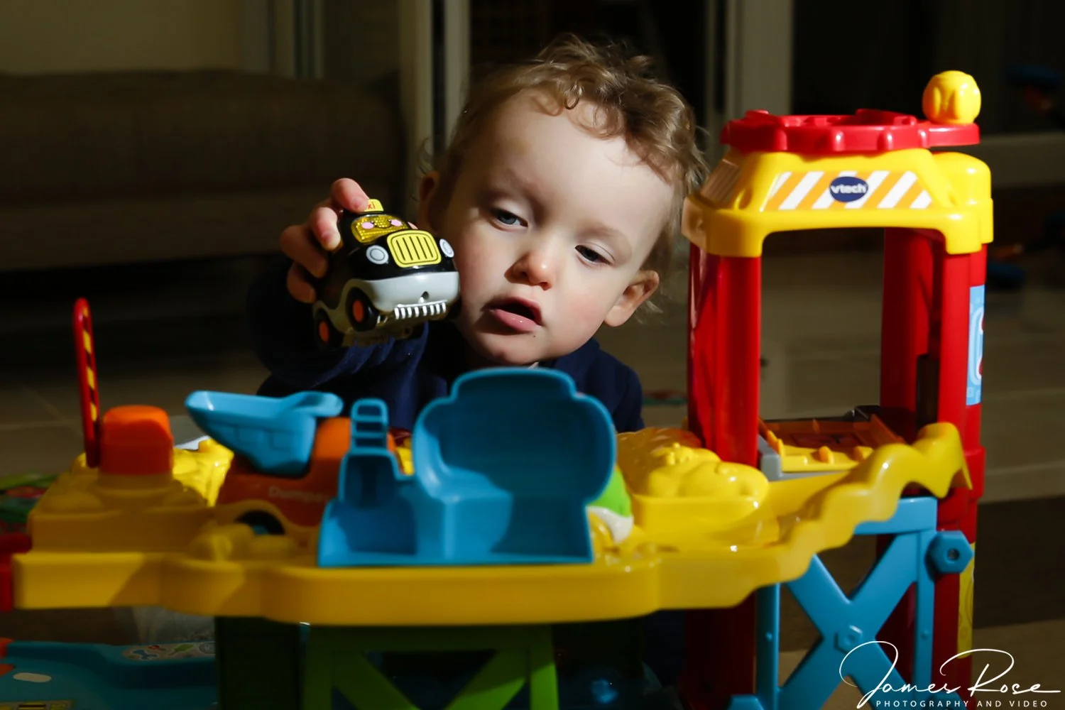 A young child playing with toy cars at a colorful playset indoors.