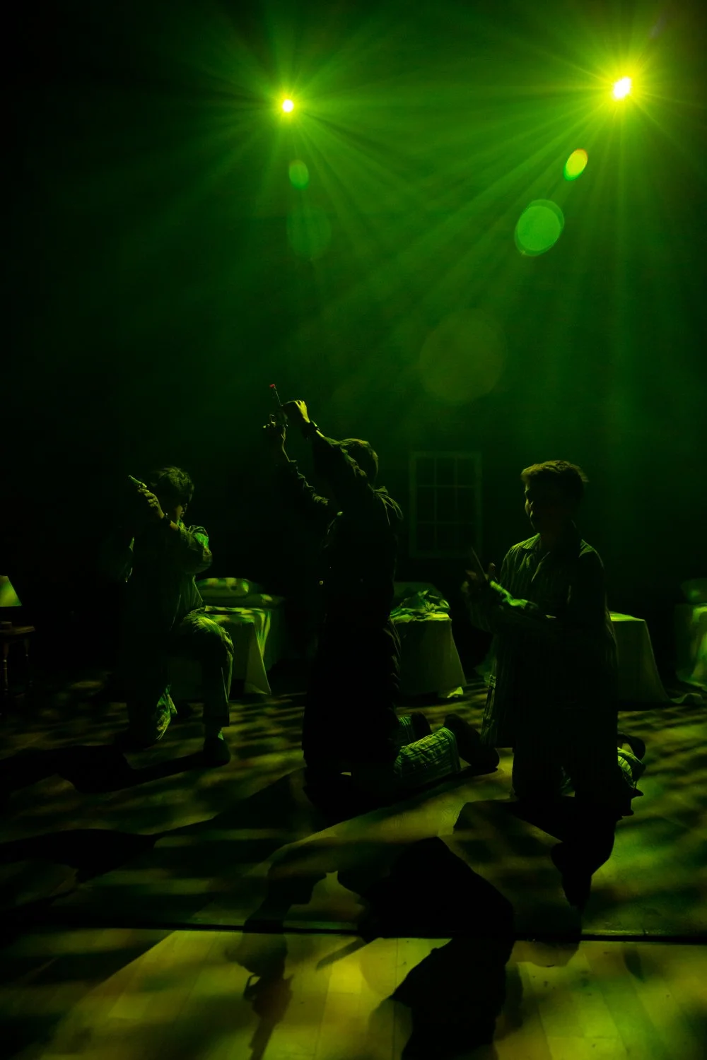 A group of people in a dark room illuminated by green stage lights, with some individuals kneeling and others standing, engaged with their phones, surrounding a person holding a device in the air.