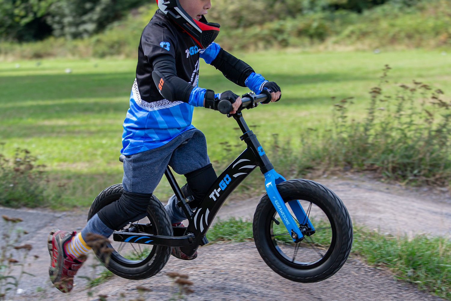 Child riding a black and blue balance bike on a dirt path in a park.