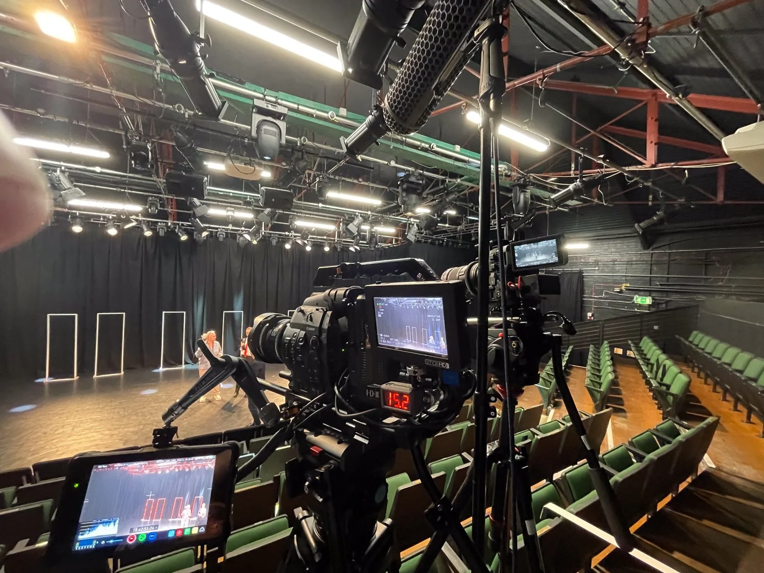 Recording studio with two cameras aimed at a small stage with black curtains, set up for filming or rehearsal.