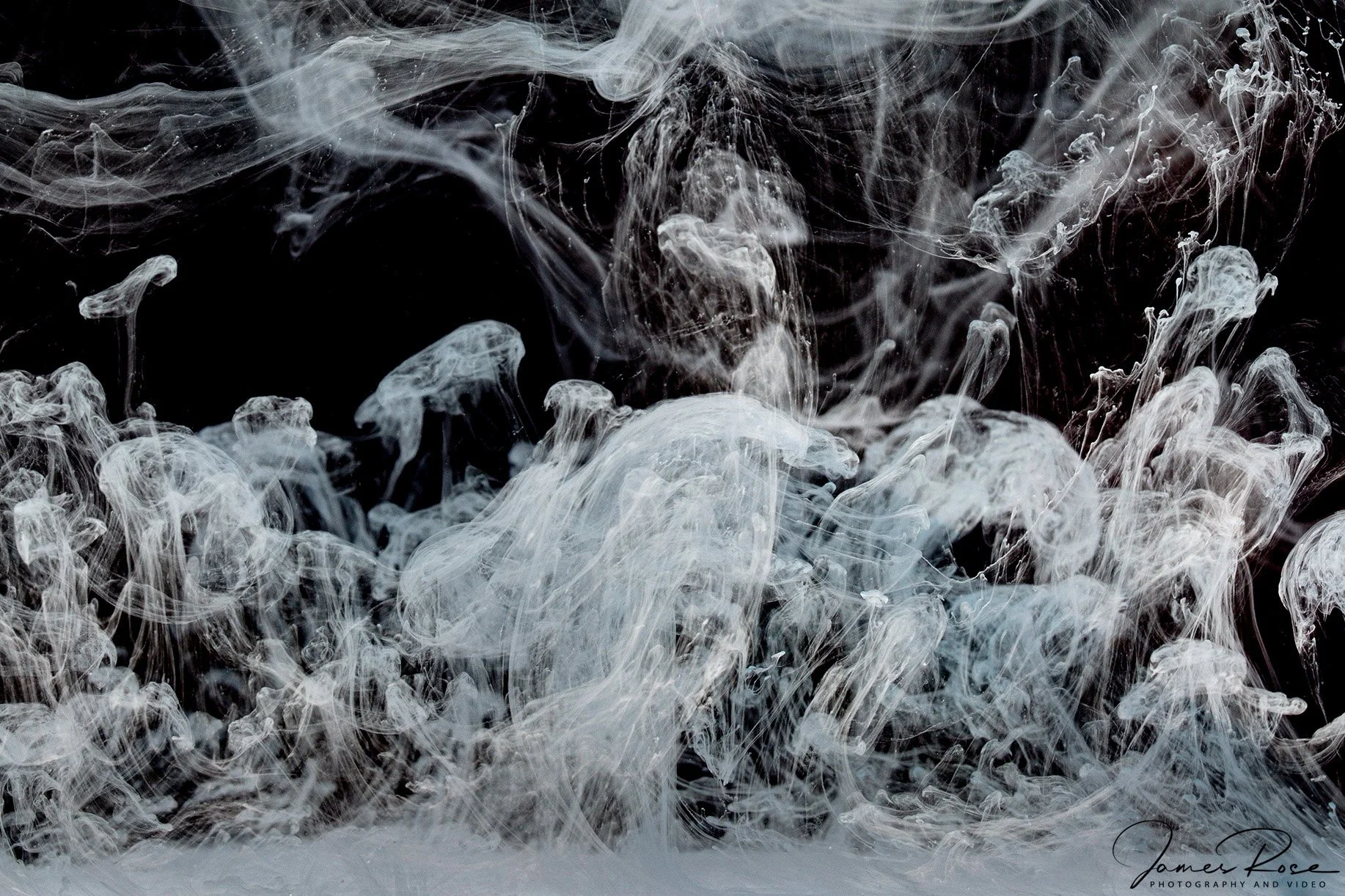 Swirling white smoke or ink in dark water creating abstract shapes and patterns.