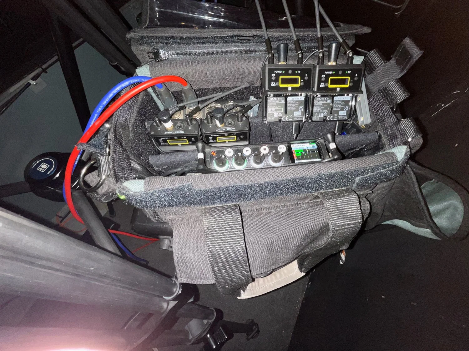 A portable radio communication device setup with multiple radios, a control panel, rechargeable batteries, and connected cables, placed in a padded carrying case.