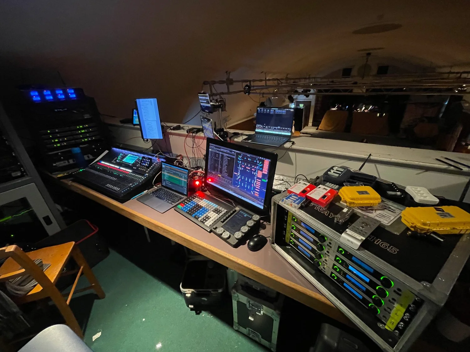 DJ equipment setup with multiple monitors, sound mixing console, and electronic devices on a table in a dimly lit environment.