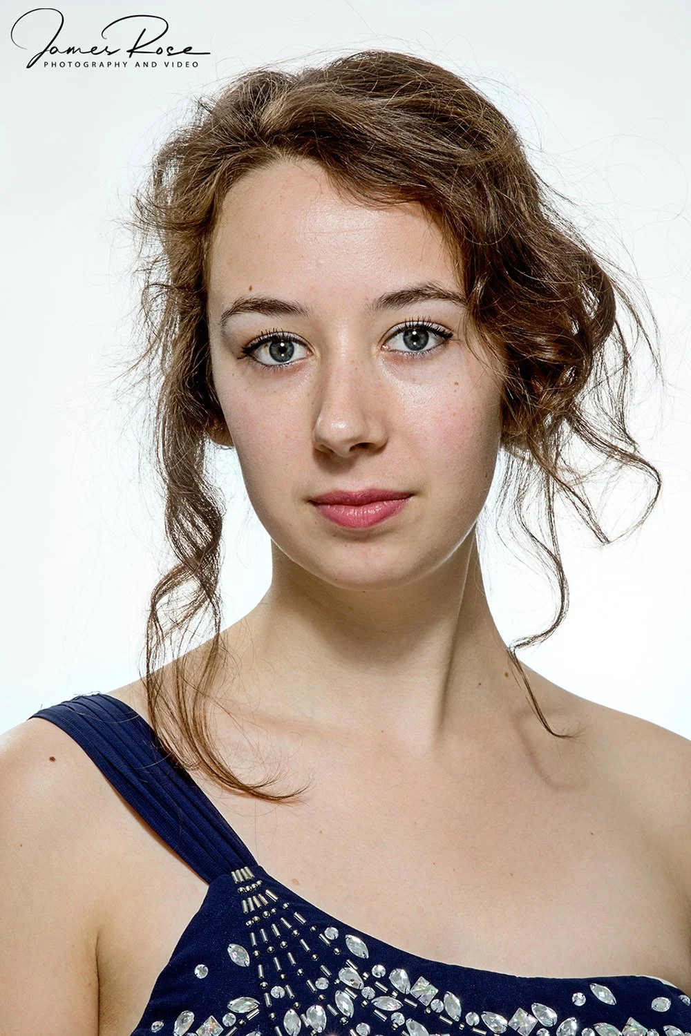 A young woman with blue eyes, red hair, and light skin wearing a dark blue dress with rhinestone embellishments.
