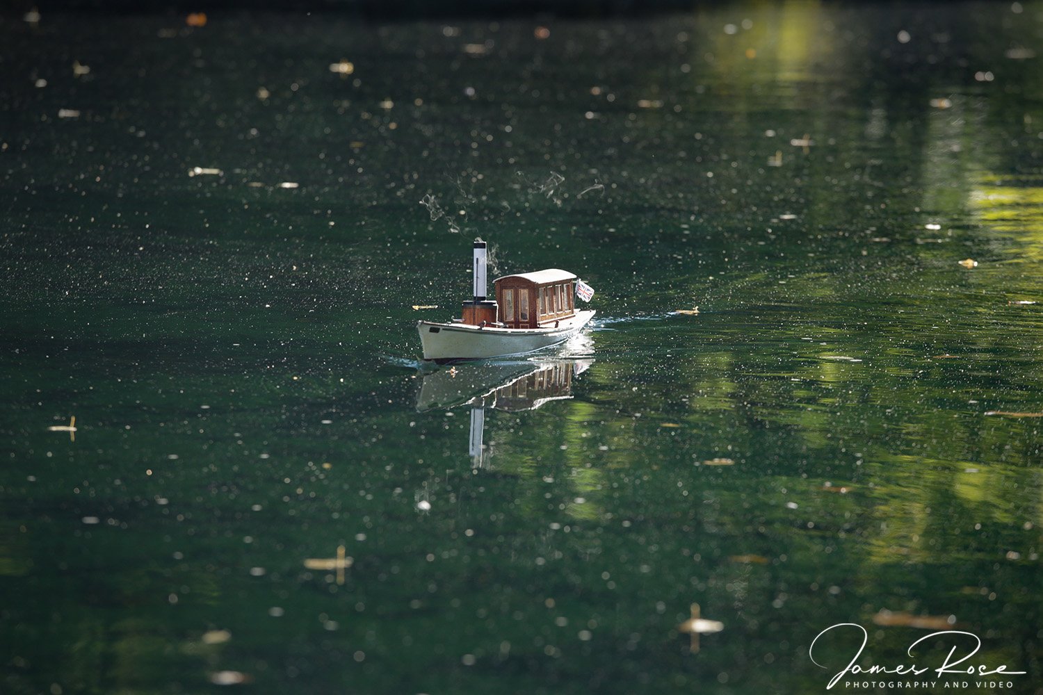Miniature boat floating on a body of water, with reflections and small floating debris