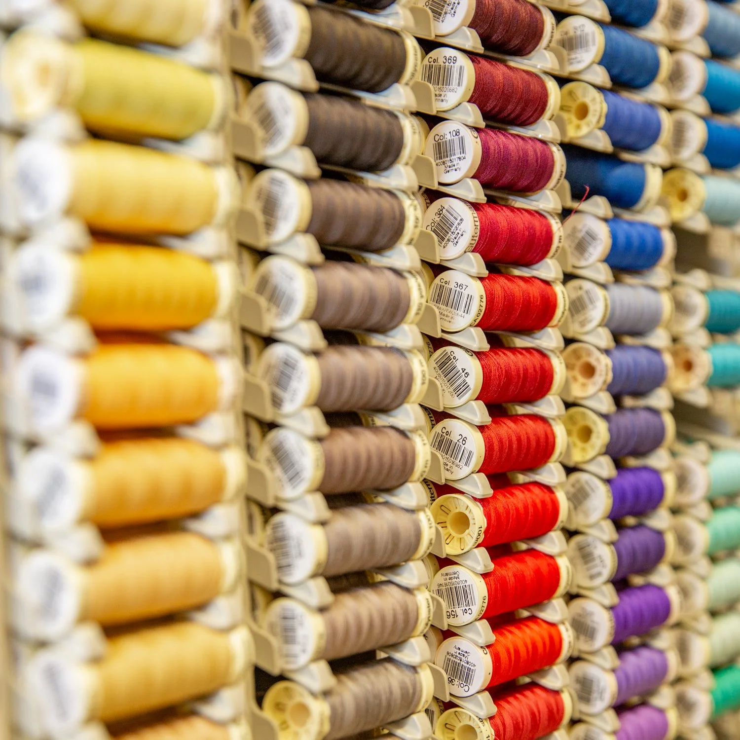 Rows of colorful sewing thread spools organized by color on display at a craft store.