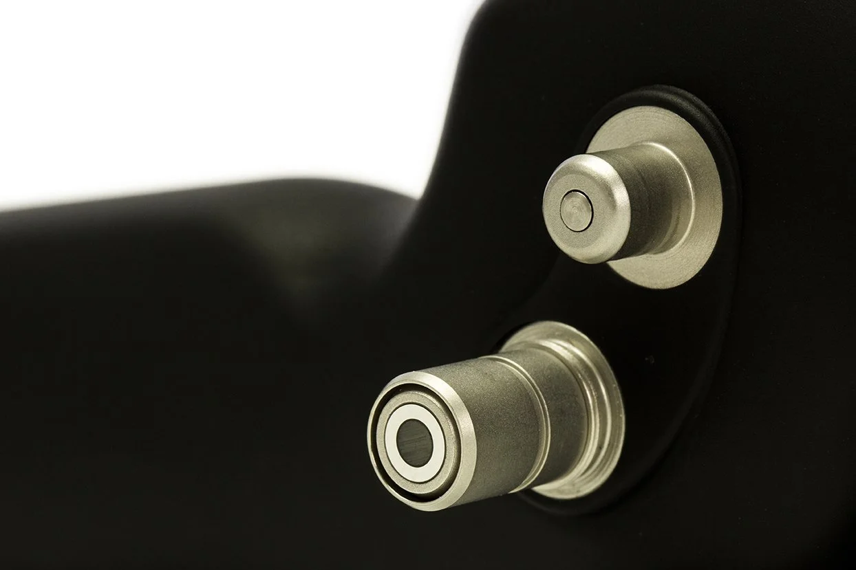 Close-up of two metallic circular ports on a black electronic device, possibly a speaker or audio equipment.