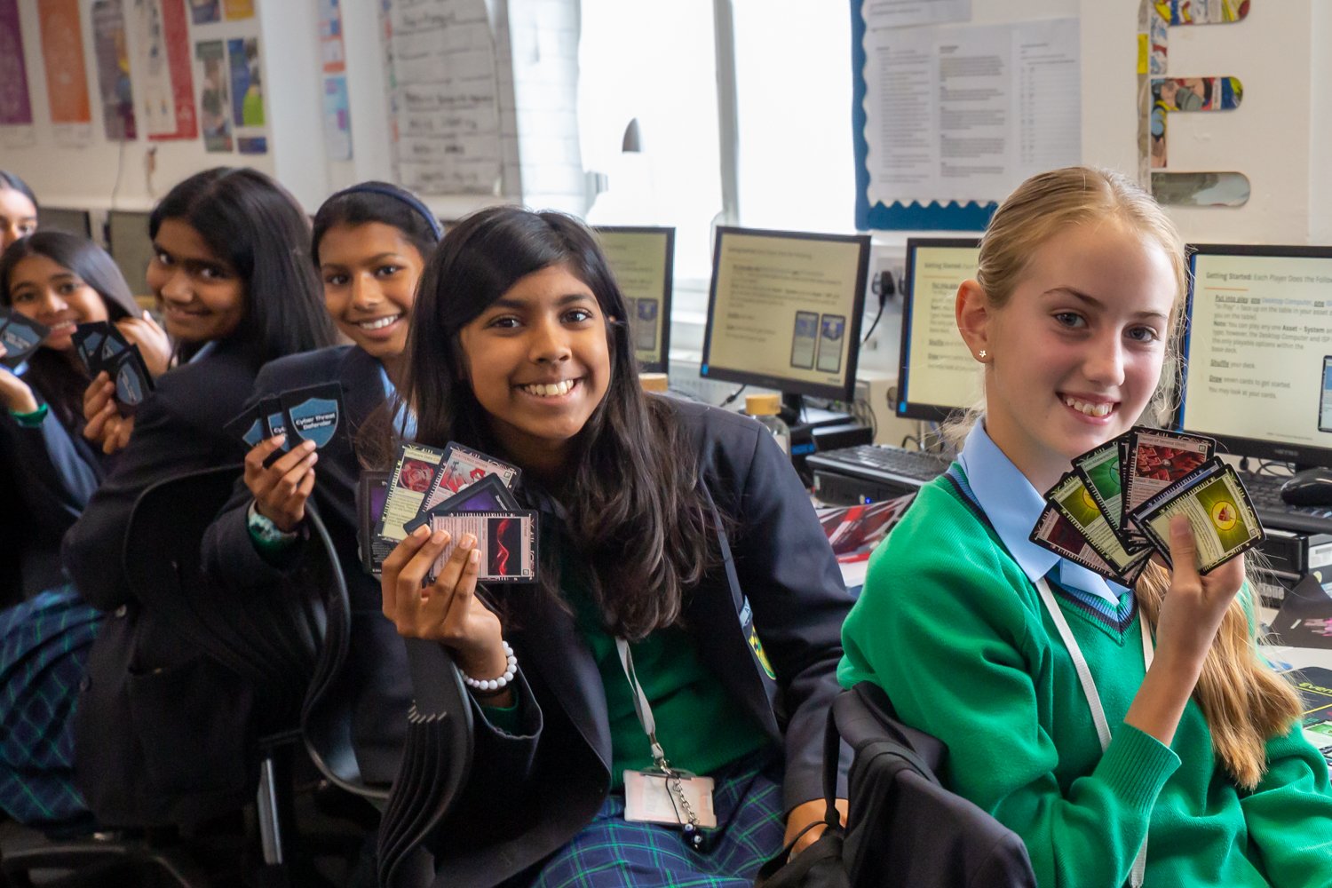 Schoolgirls smiling and holding trading cards in a computer lab classroom.