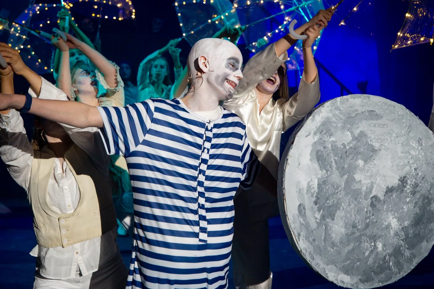 People dressed as mimes performing in a theatrical show with moon and stars decorations in the background.