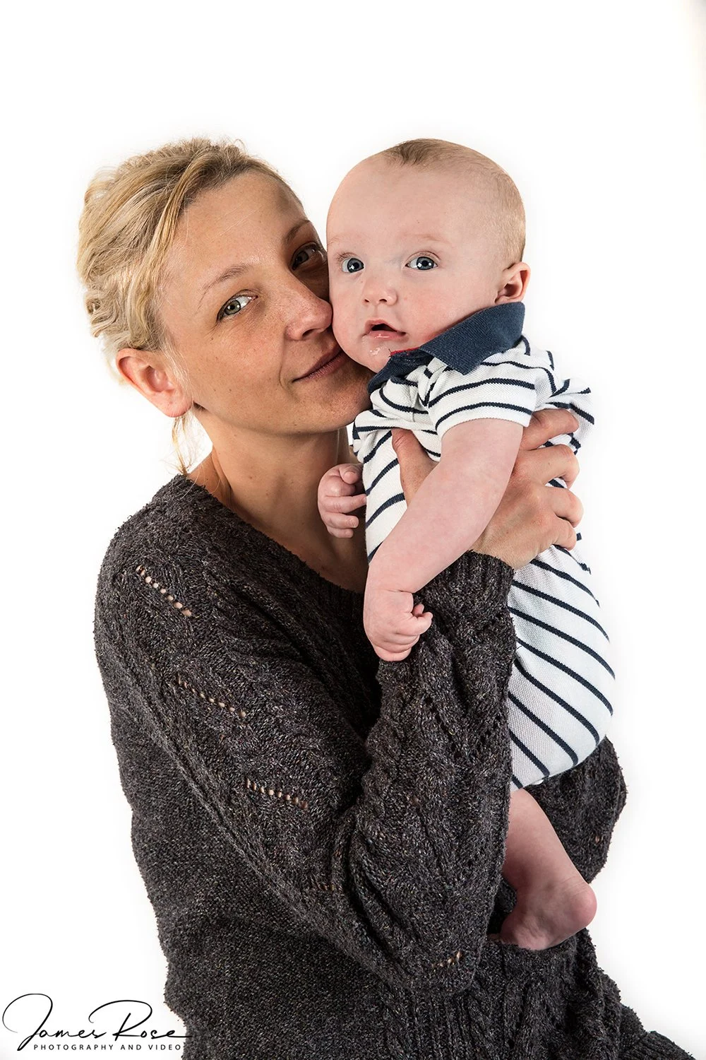 A woman holding a baby boy with light hair and blue eyes, both looking at the camera, against a white background.