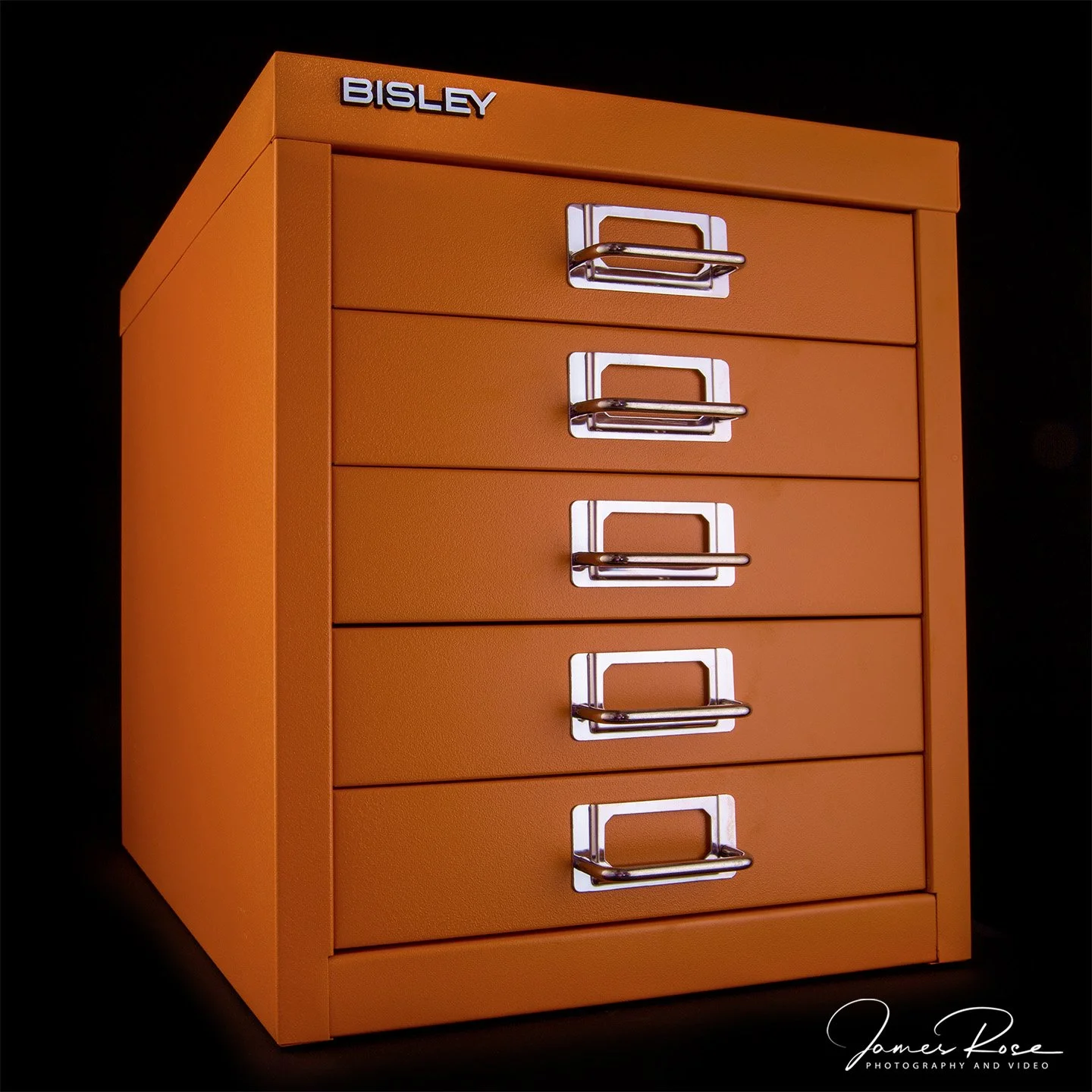 Orange metal filing cabinet with five drawers, each with a silver handle, against a black background, and the brand name 'BISLEY' on the top left corner.