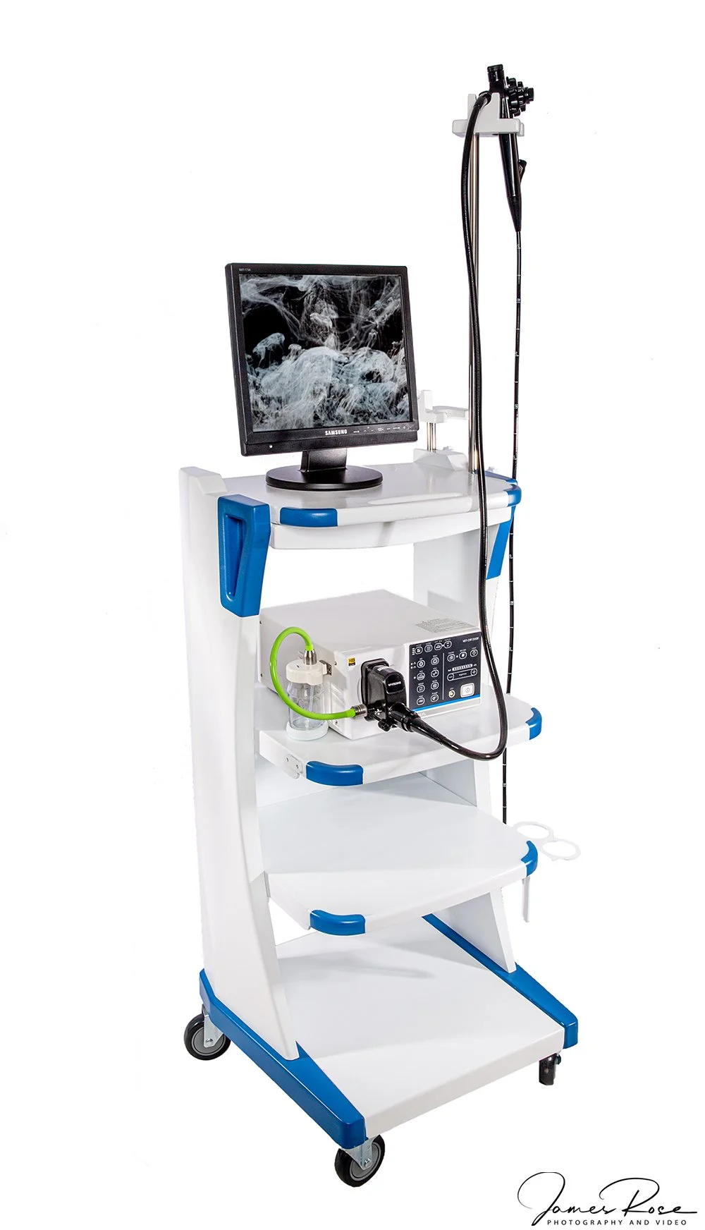 Medical equipment cart with a computer monitor, an endoscope, and various medical devices on white background.