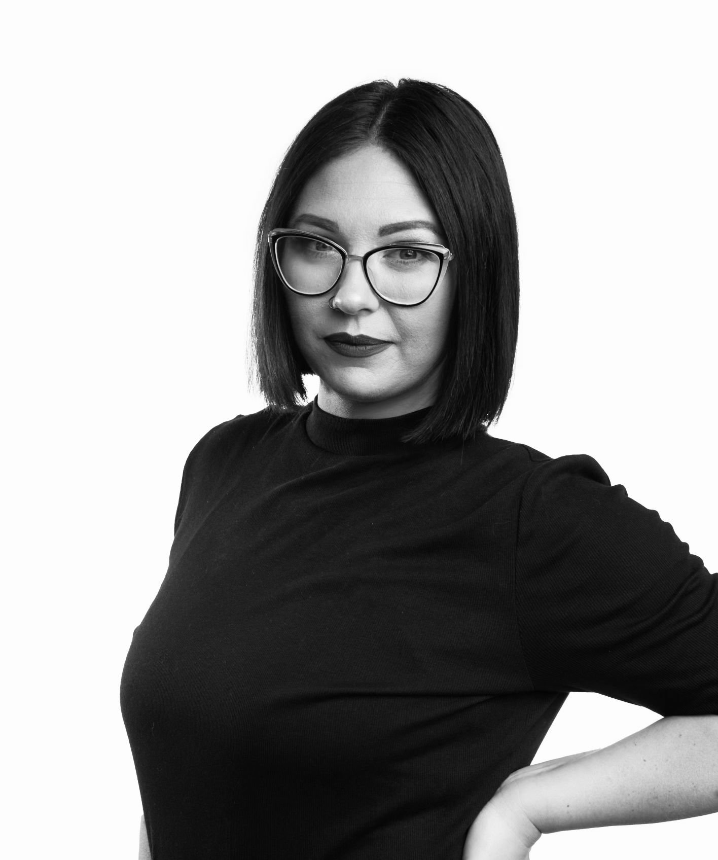 A woman with shoulder-length dark hair, glasses, and dark lipstick posing against a plain white background.