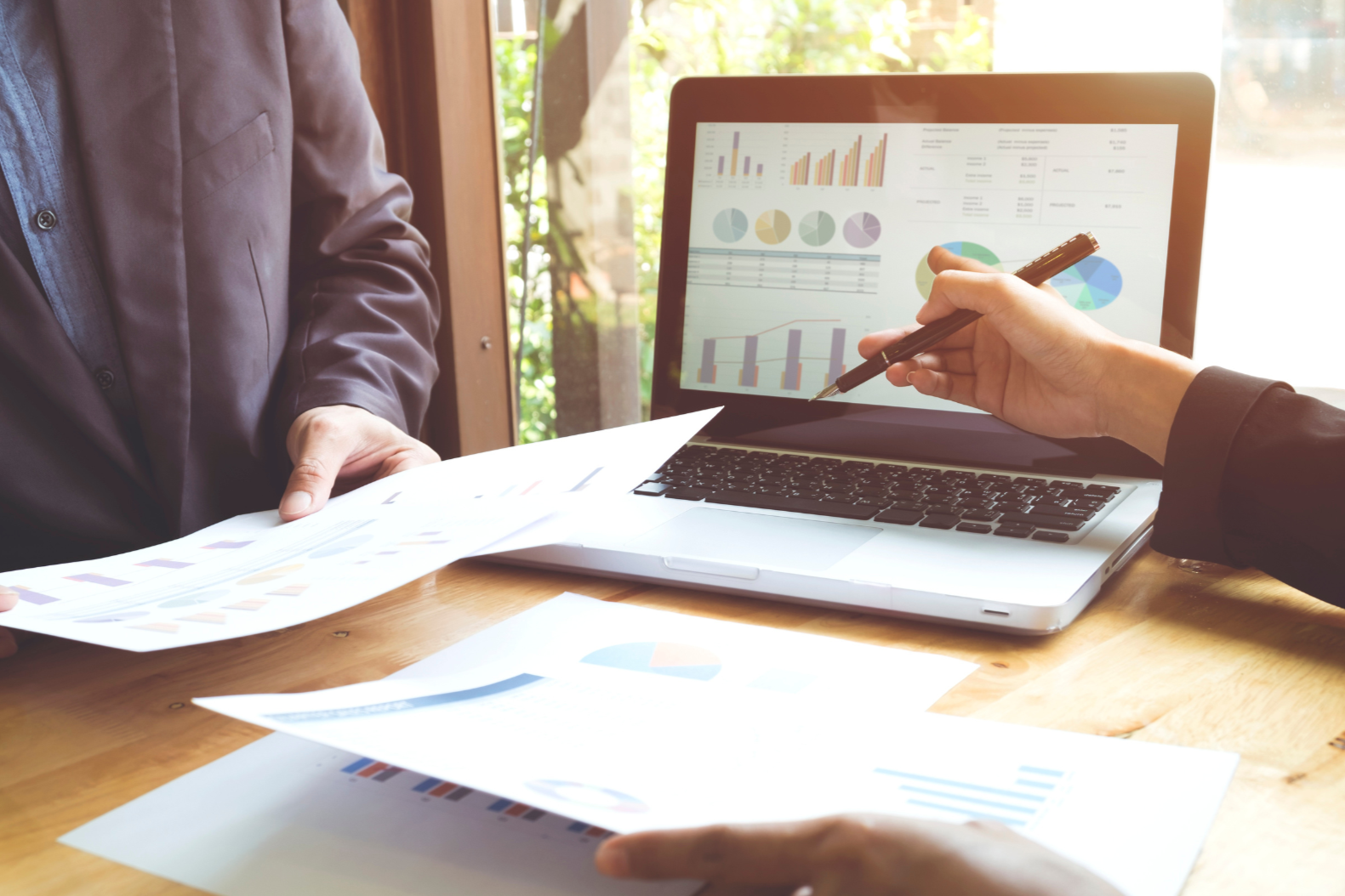 Two people reviewing financial documents and analyzing graphs on a laptop screen during a meeting.