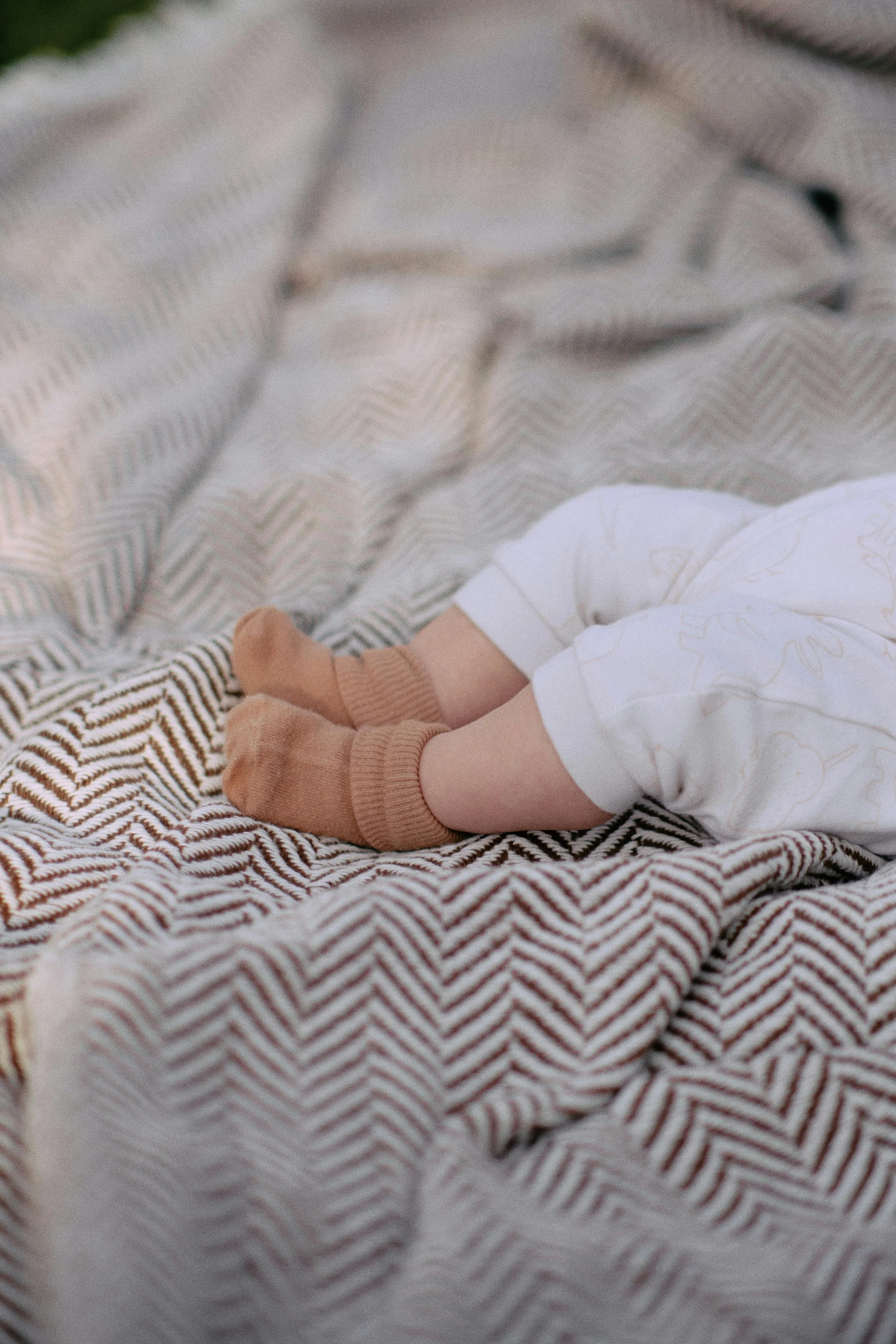 Close-up of a baby's legs wearing beige socks, lying on a patterned blanket.