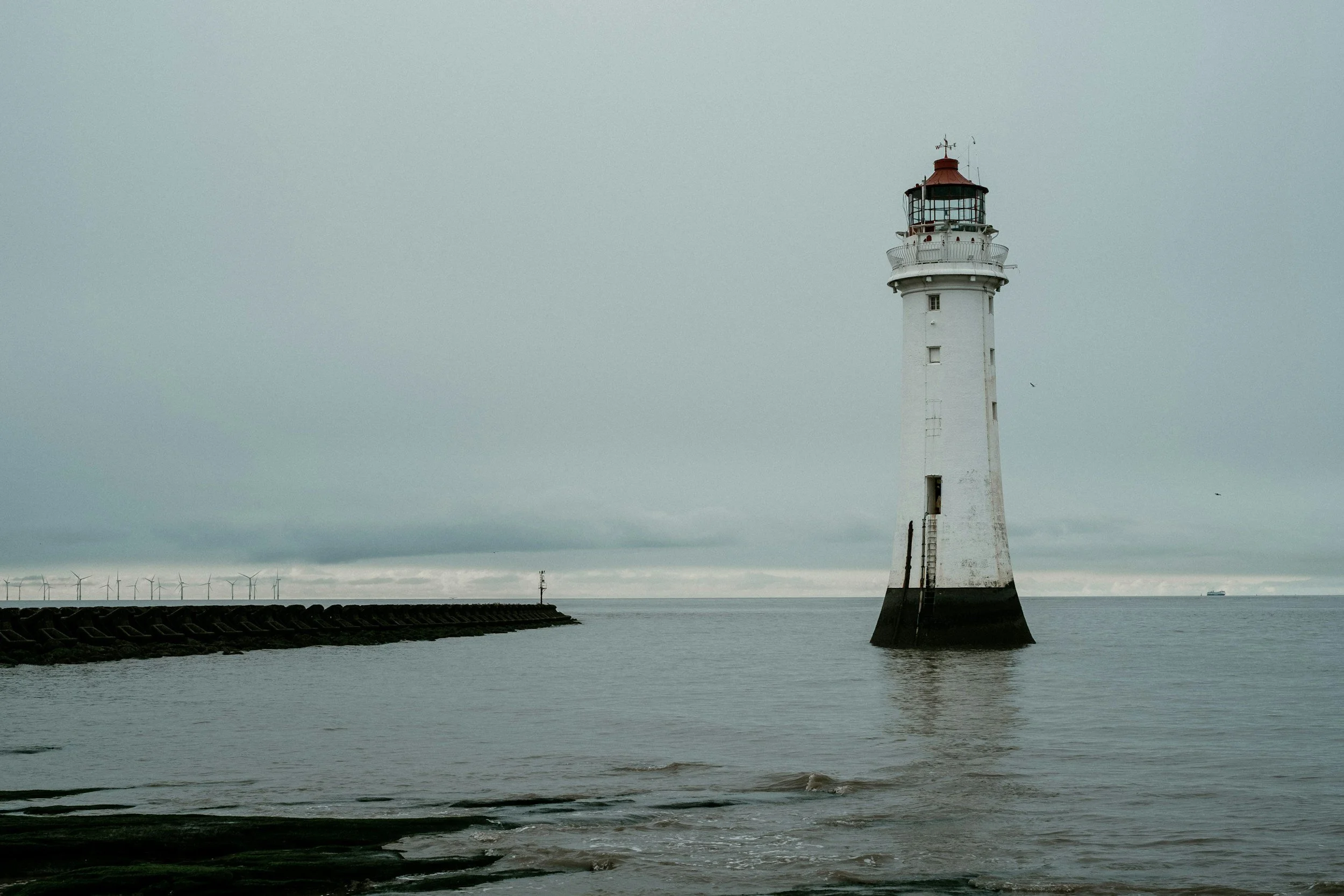 A lighthouse in the ocean near a breakwater, under a cloudy sky.