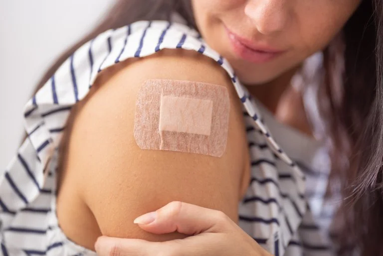 Close-up of a woman with a bandage on her upper arm after receiving a vaccination.