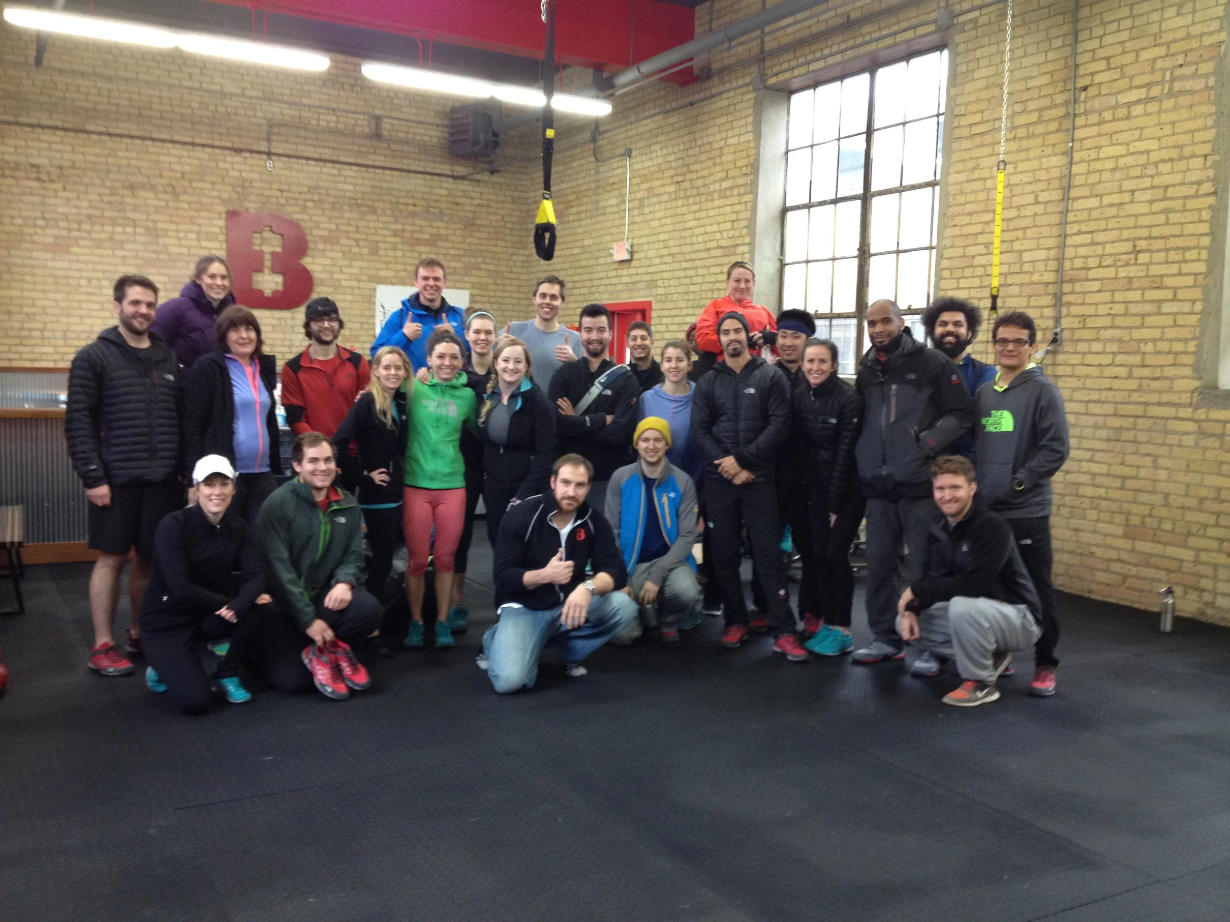 Group of people in a gym posing for a photo, some smiling and giving thumbs up.