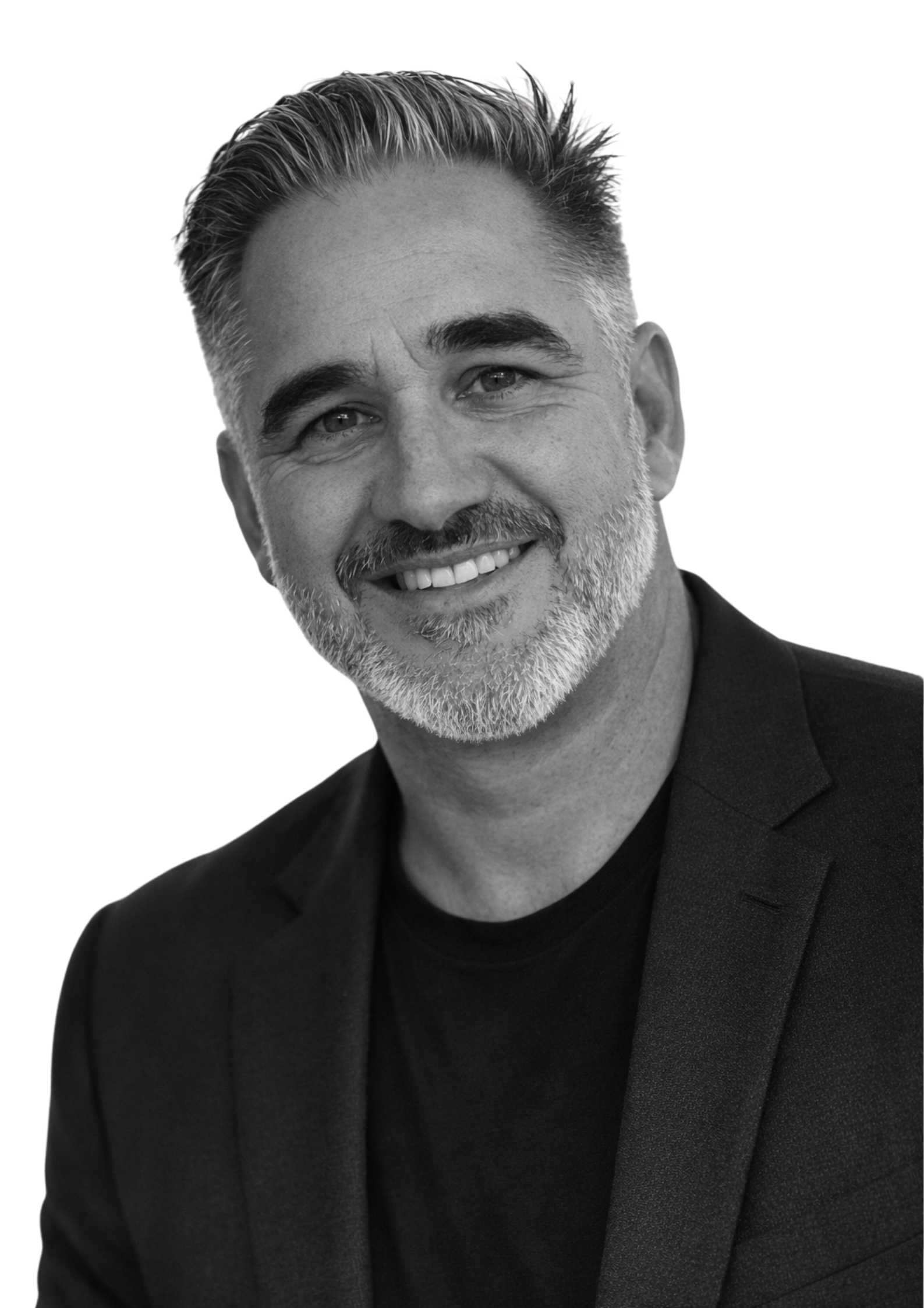 Black and white portrait of a smiling middle-aged man with gray hair and beard, wearing a suit jacket and a black shirt.