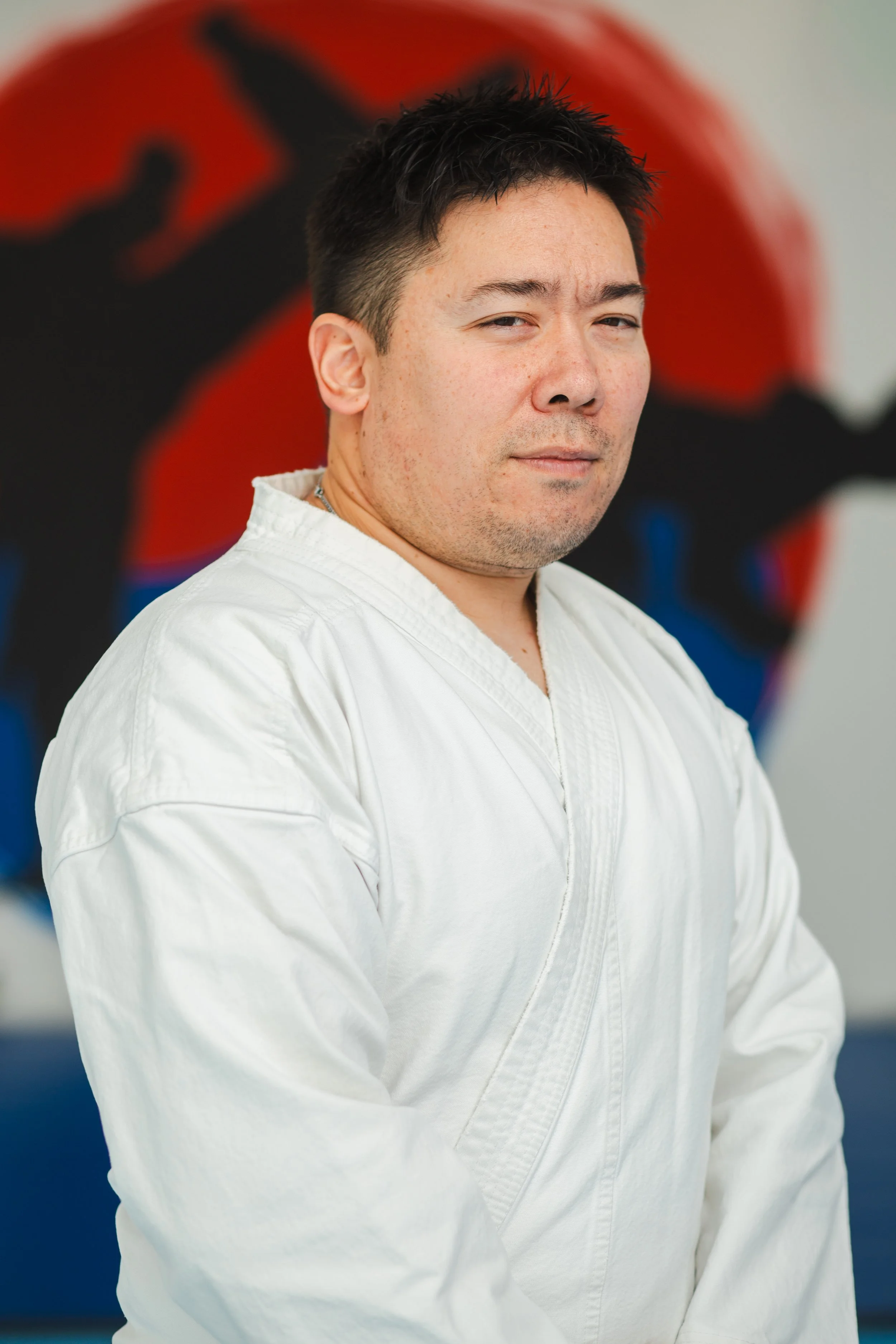 A man in a white martial arts uniform standing in front of a colorful background.
