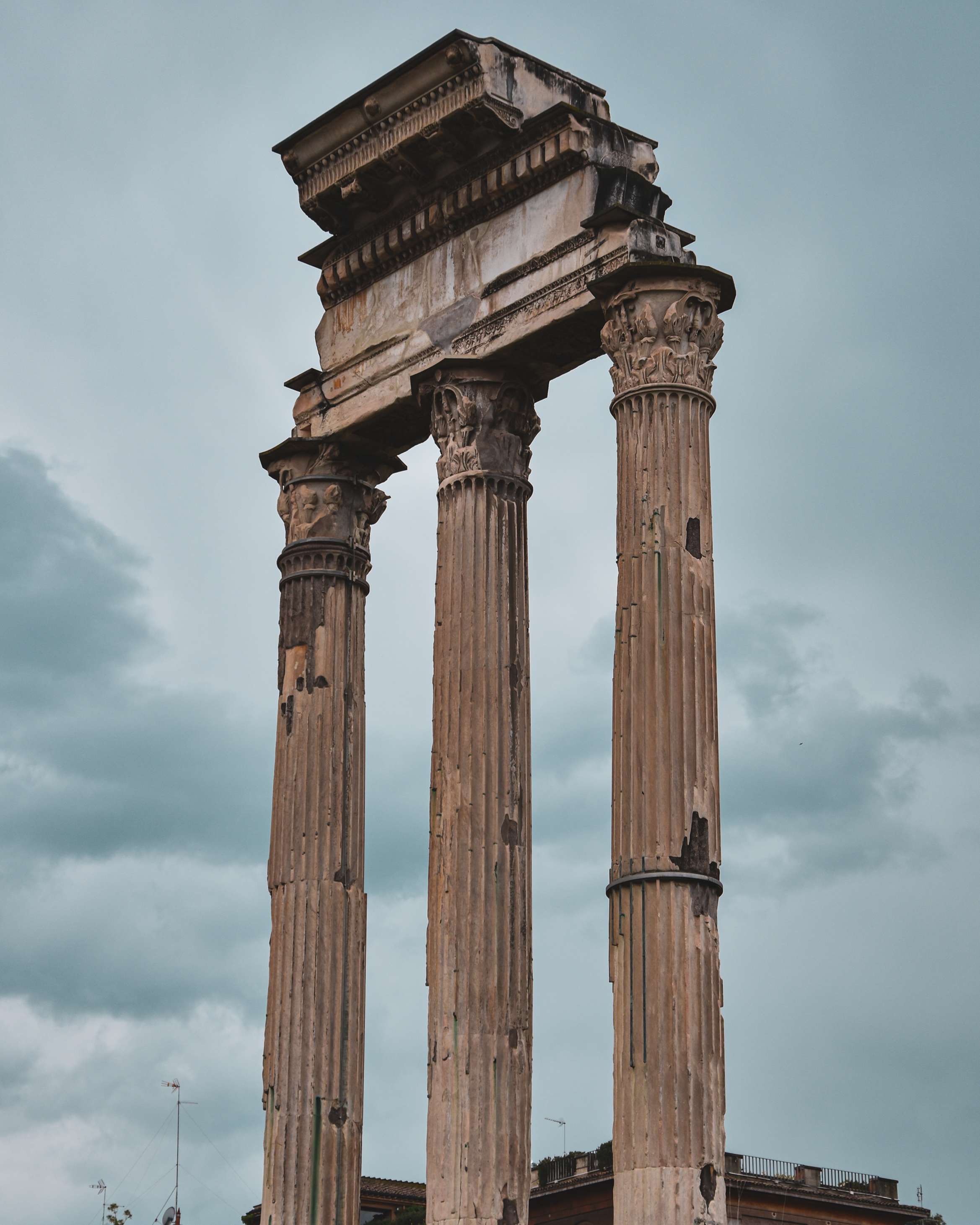 Ancient Roman ruins with three tall, weathered columns under a cloudy sky.