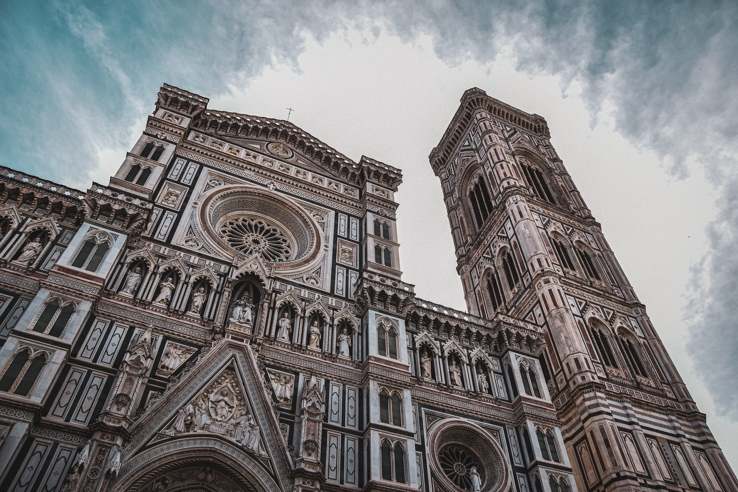 Low-angle view of the ornate Florence Cathedral with its adjacent bell tower on a cloudy sky day.