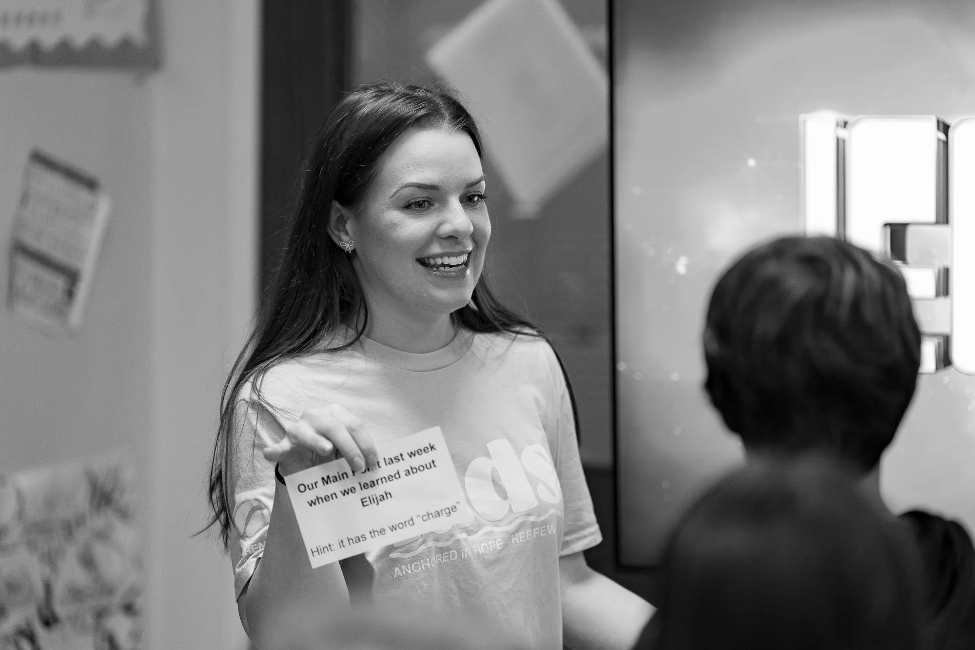 A woman smiling and holding a paper while talking to a man in an indoor setting.