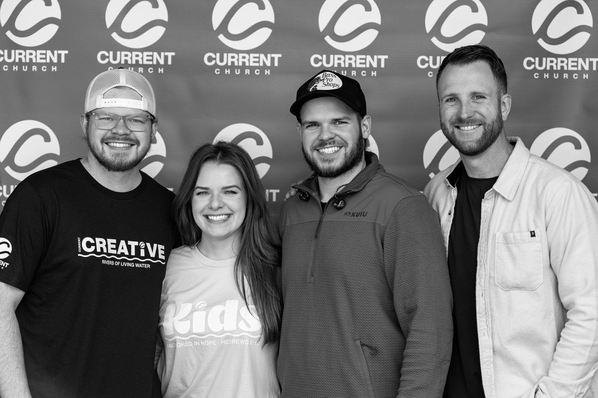 Group of four smiling adults standing in front of a backdrop with 'Current Church' logos.
