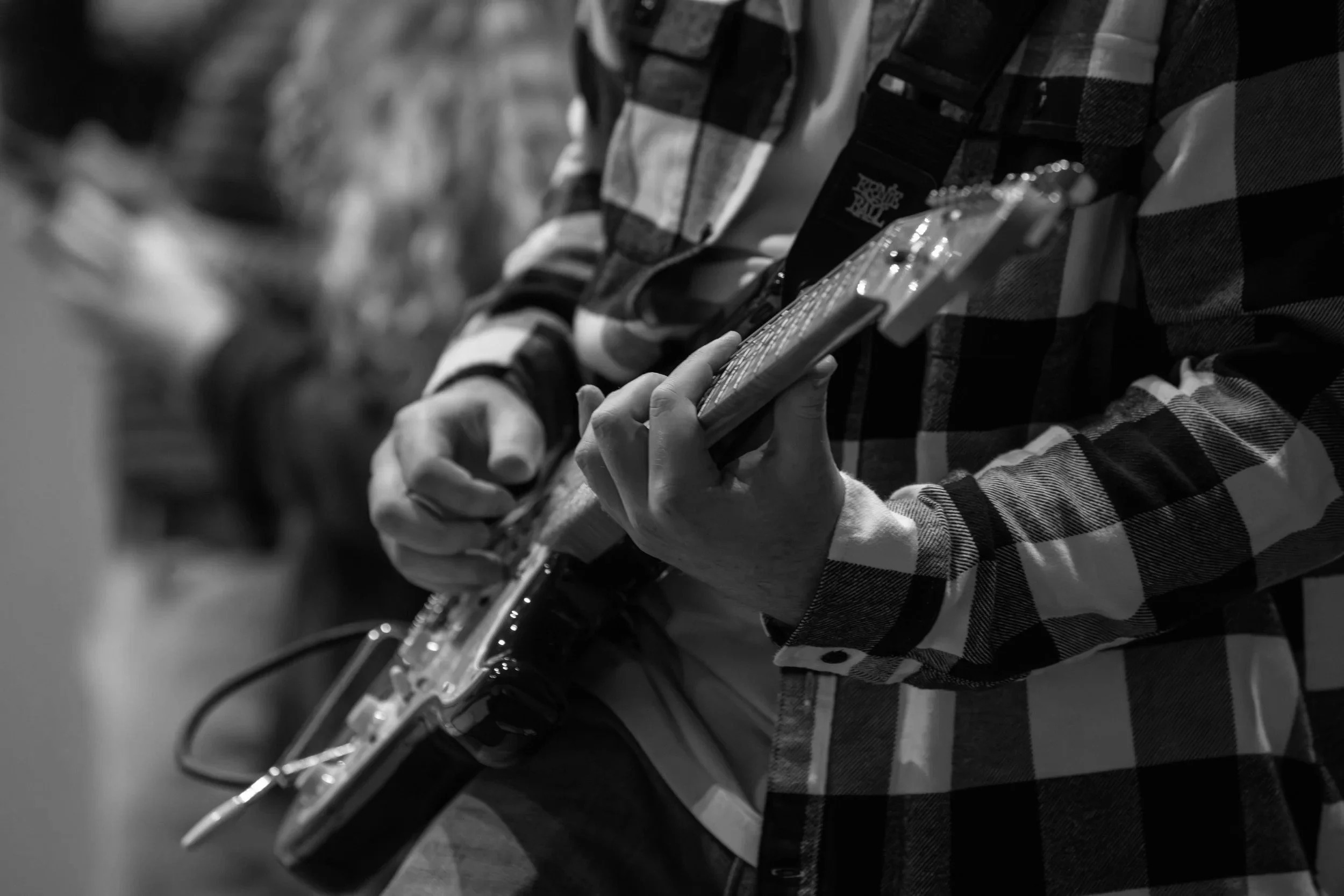 Person playing an electric guitar, wearing a checkered shirt. Focus on their hands and the guitar.