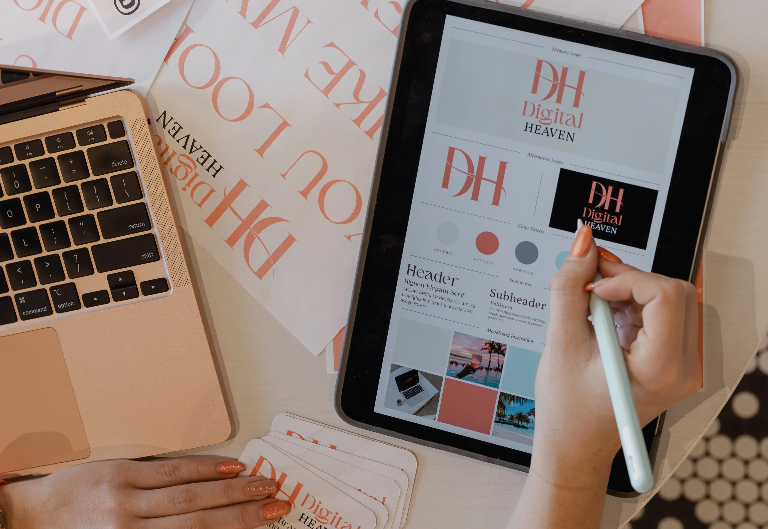 Nevaeh owner of Digital Heaven using a tablet to view logo design ideas labeled 'Digital Heaven' with color palettes, fonts, and images, surrounded by printed branding materials and a laptop on a white table.