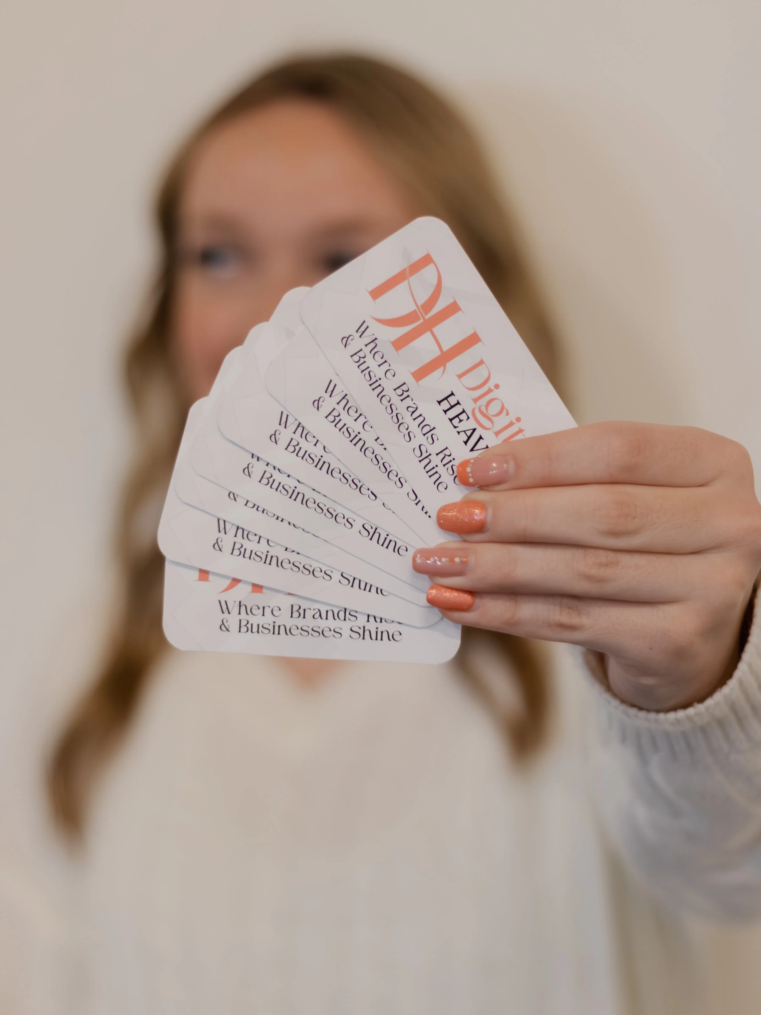 Nevaeh owner of Digital Heaven holding multiple business cards in front of their face, with the cards partially covering their features.