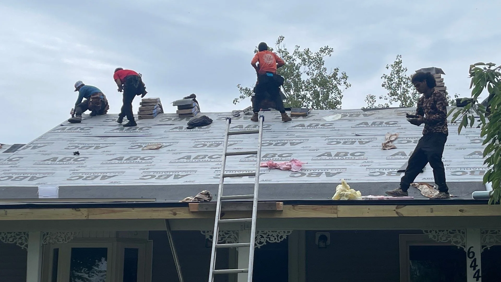 Construction workers installing roofing on a house, working on a sloped roof with insulation and roofing materials.