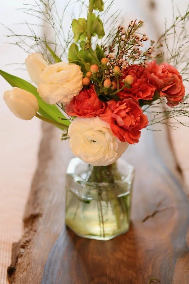 A bouquet of white and coral flowers in a clear glass vase on a wooden surface.