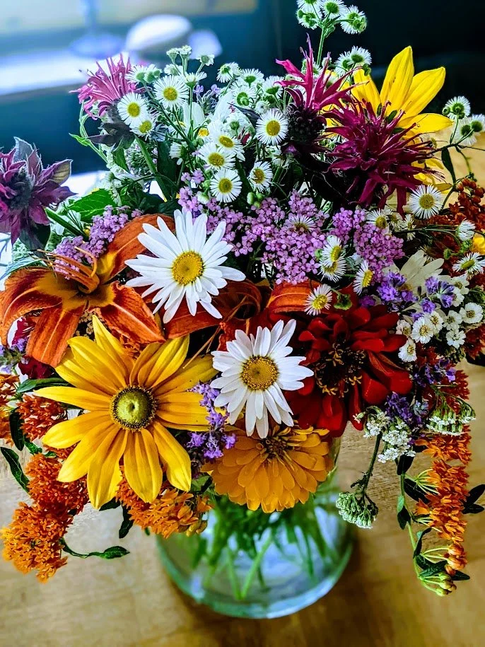 Colorful mixed flower bouquet in a glass vase on a wooden table.