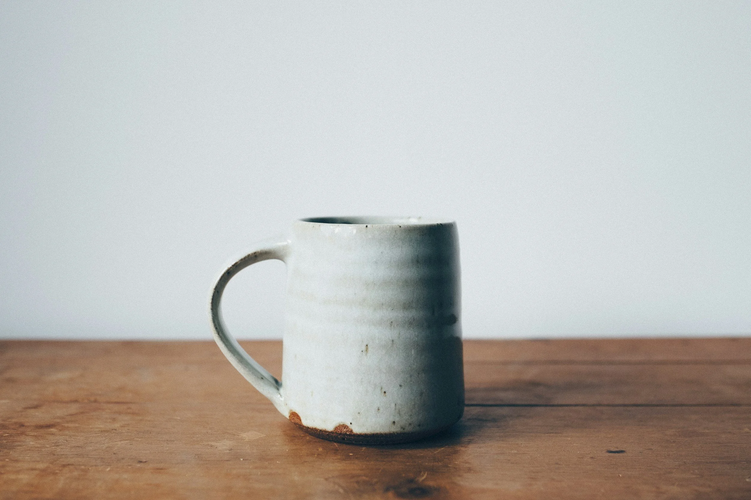 A white ceramic mug on a wooden surface against a plain white background.