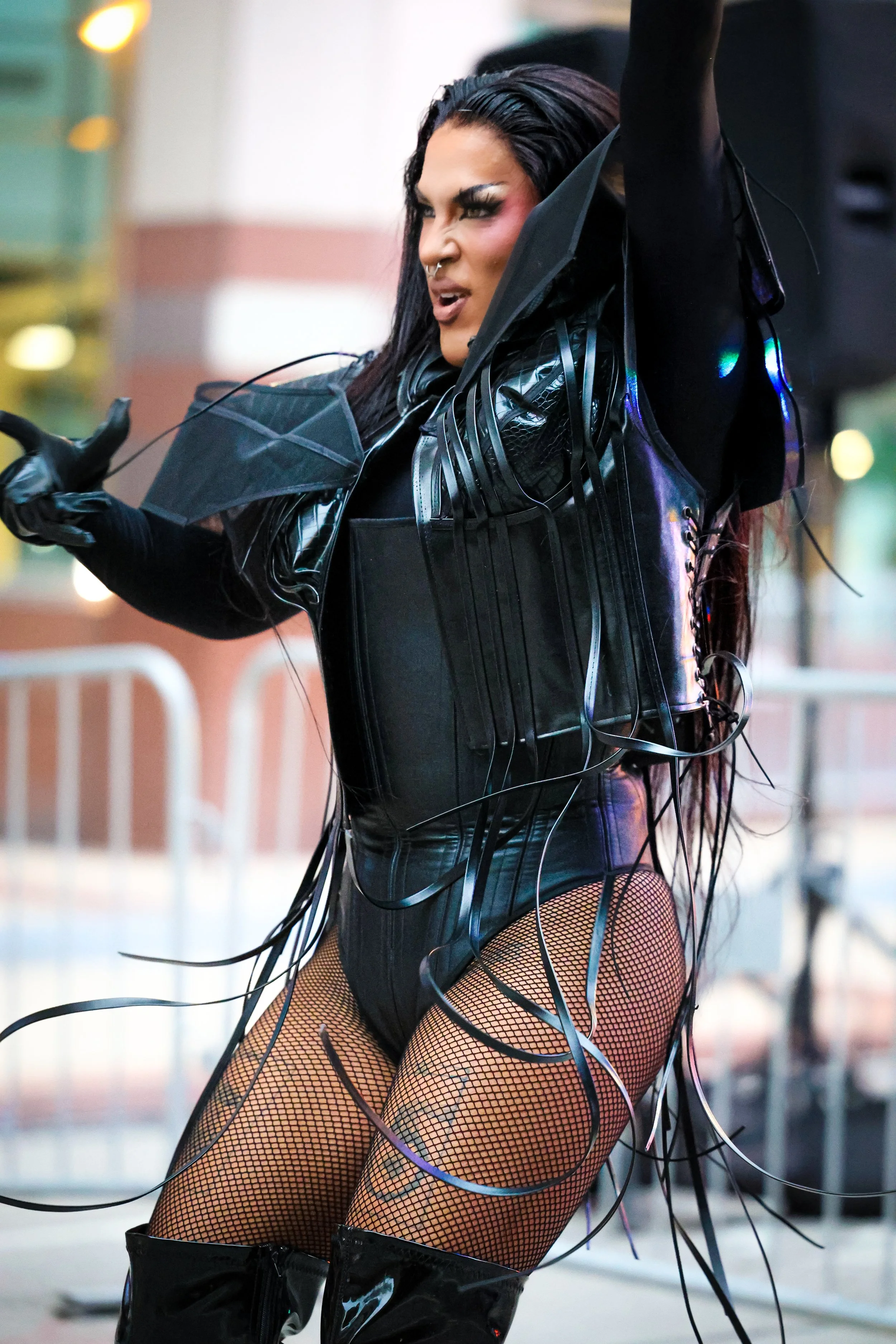 Female performer in black leather outfit with fishnet stockings, performing with wires and fabric on a stage.